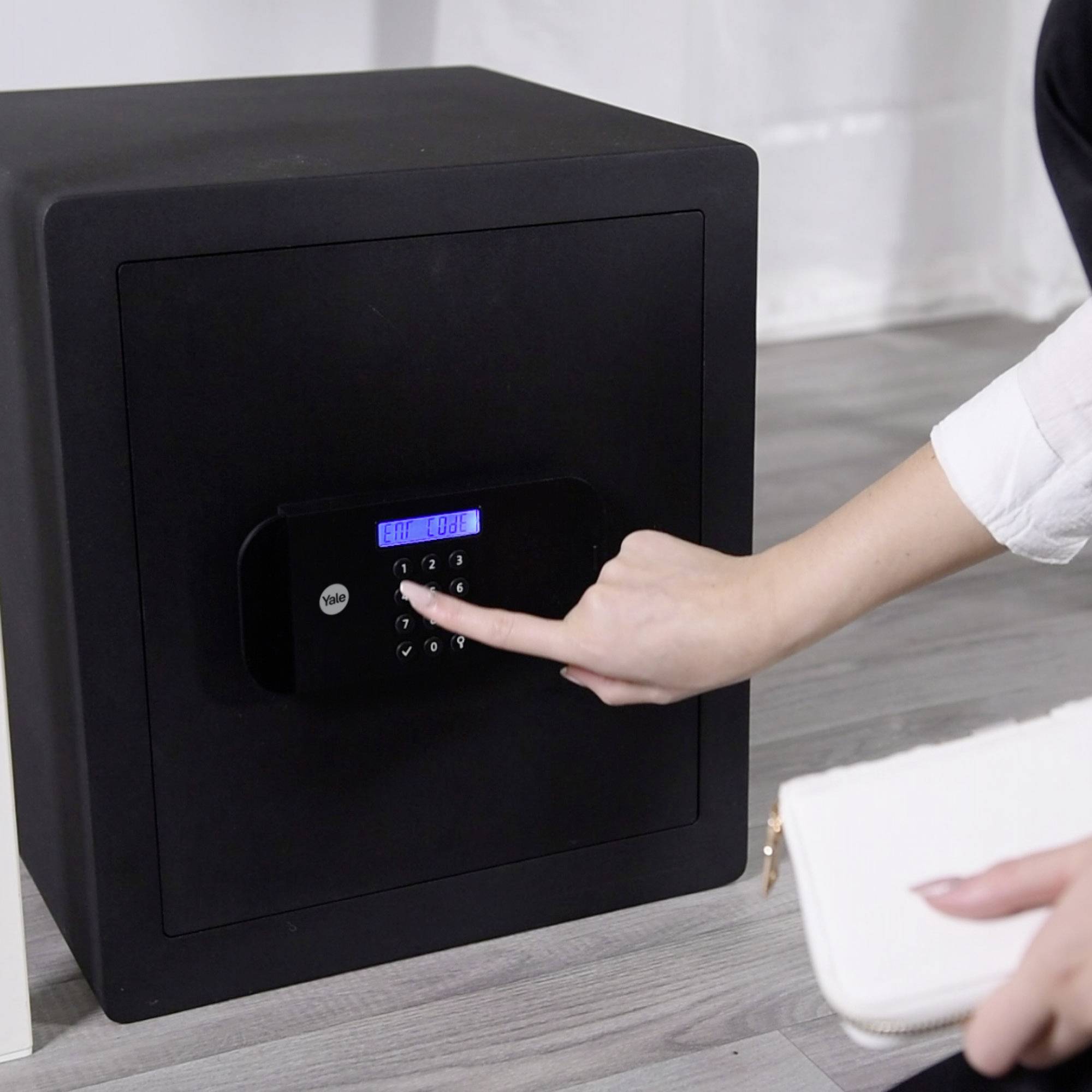 A person is typing a number combination into an electronic lock on a black safe.