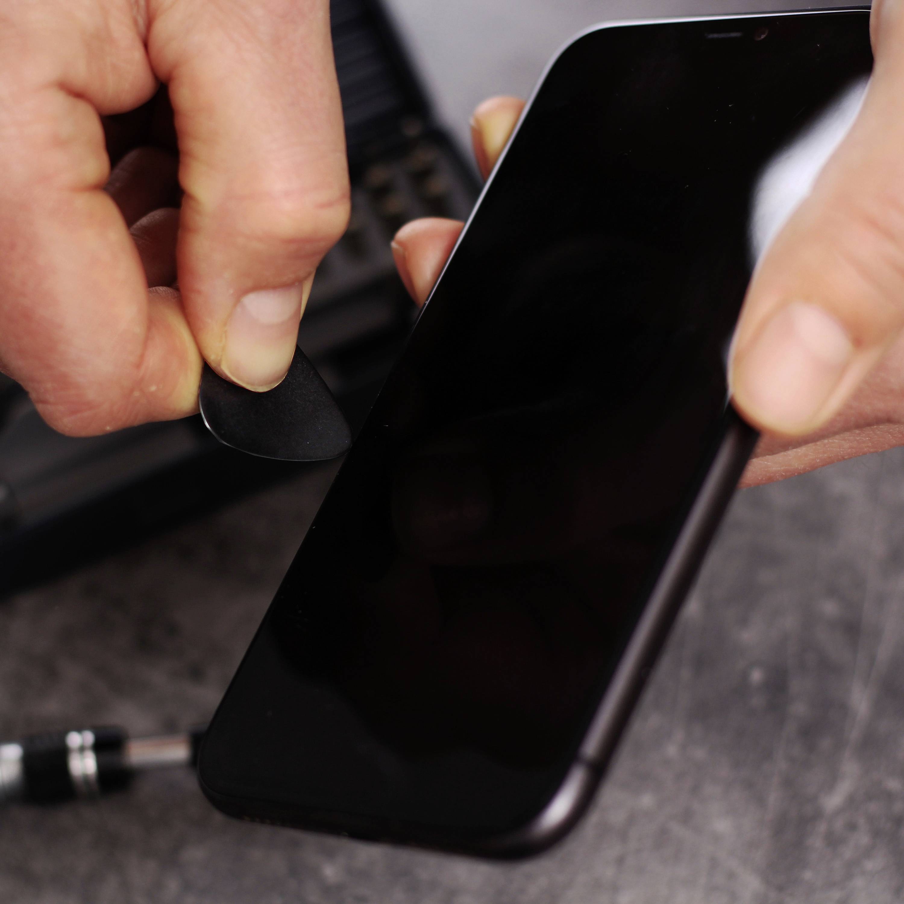 A person is using a small tool to open the display of a smartphone. Focused on repair or maintenance.