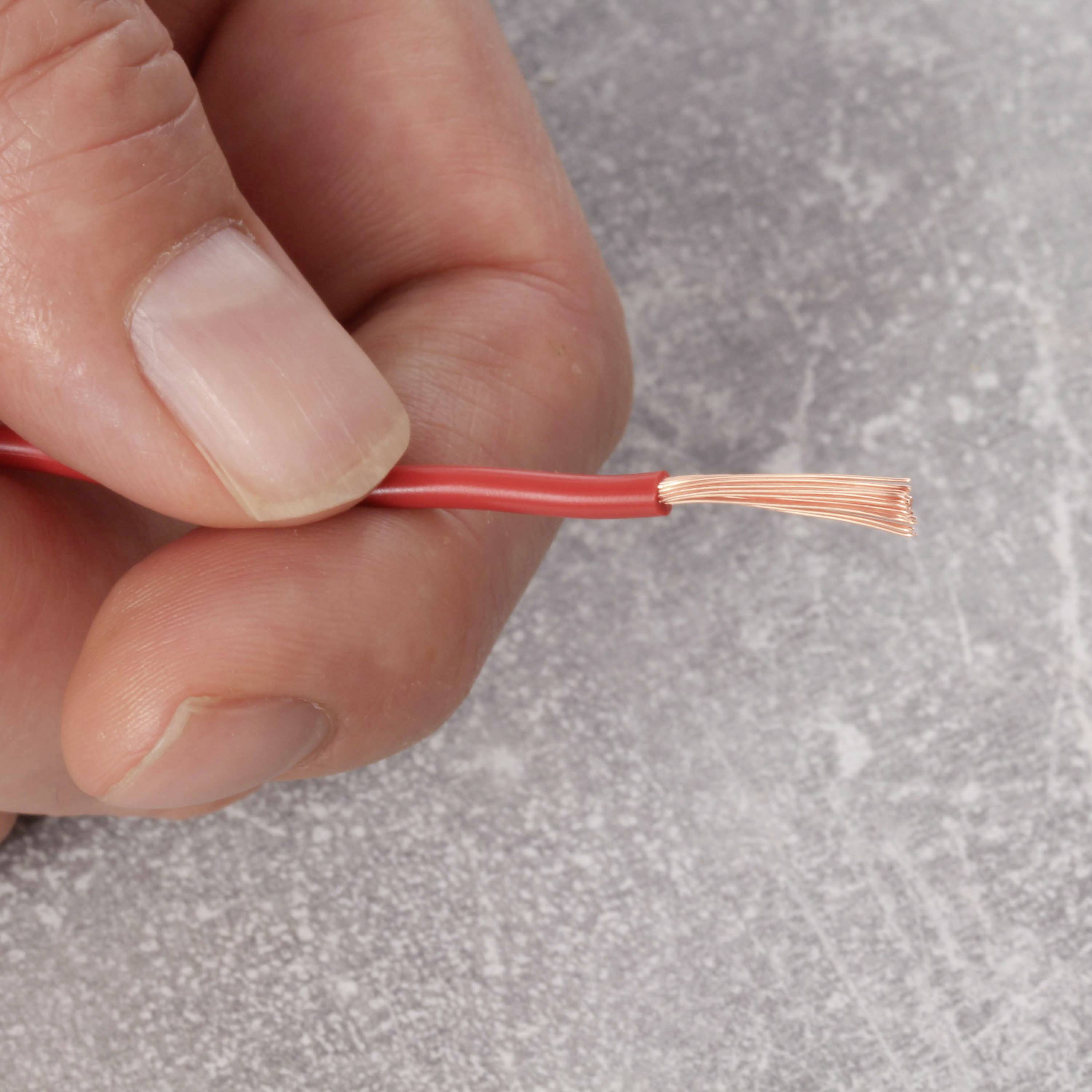 A hand is holding a red electrical cable with an exposed copper wire end against a grey background.