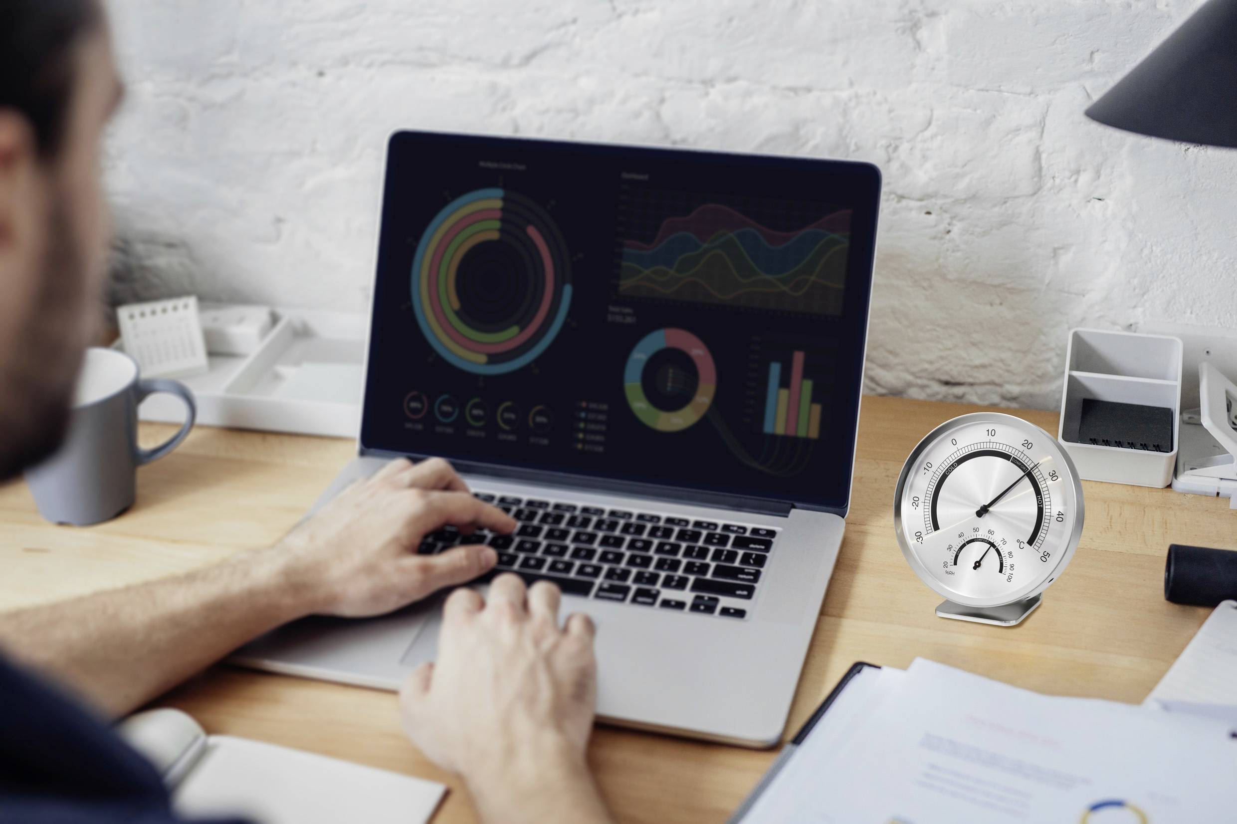 A person is working on a laptop with data visualisations and graphics. A dashboard is positioned on the right side of the table.