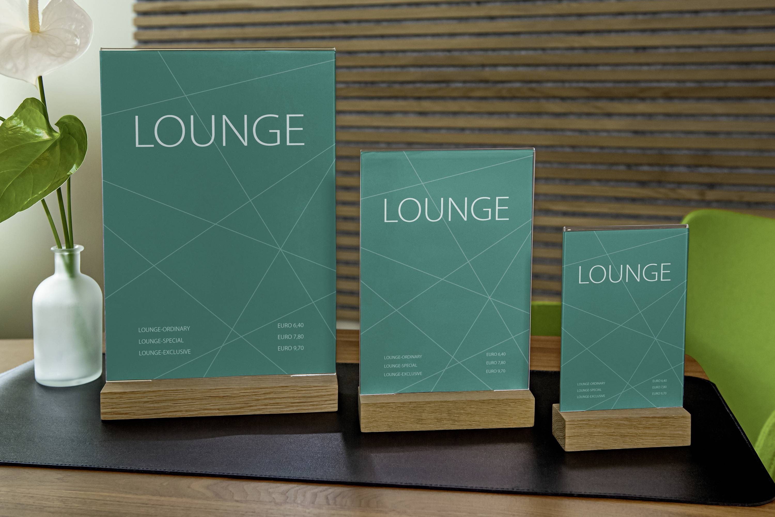 Three turquoise table displays with the text 'LOUNGE' stand on wooden bases in front of a wooden wall. They are of different sizes.