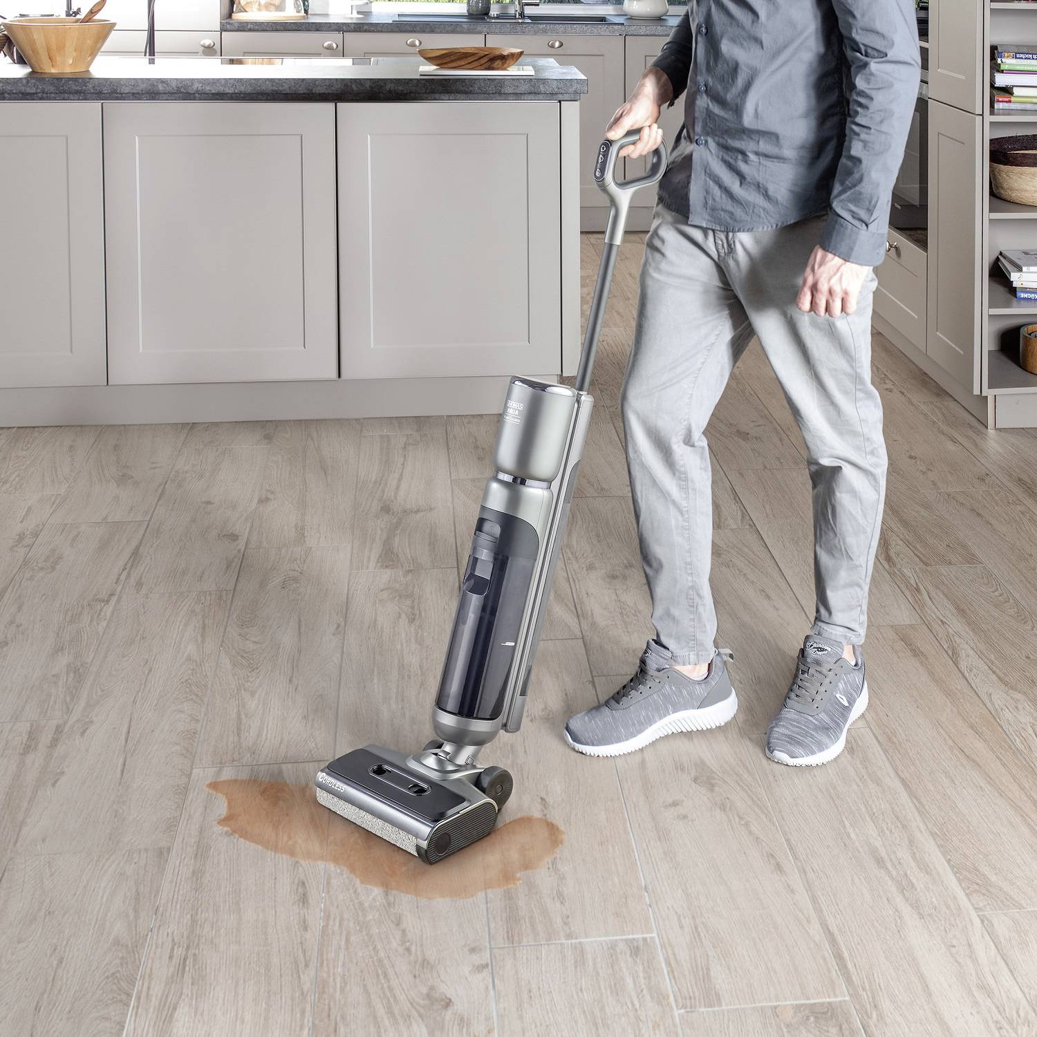A person is cleaning a wooden floor with a wet vacuum cleaner where a liquid has been spilt in a modern kitchen.