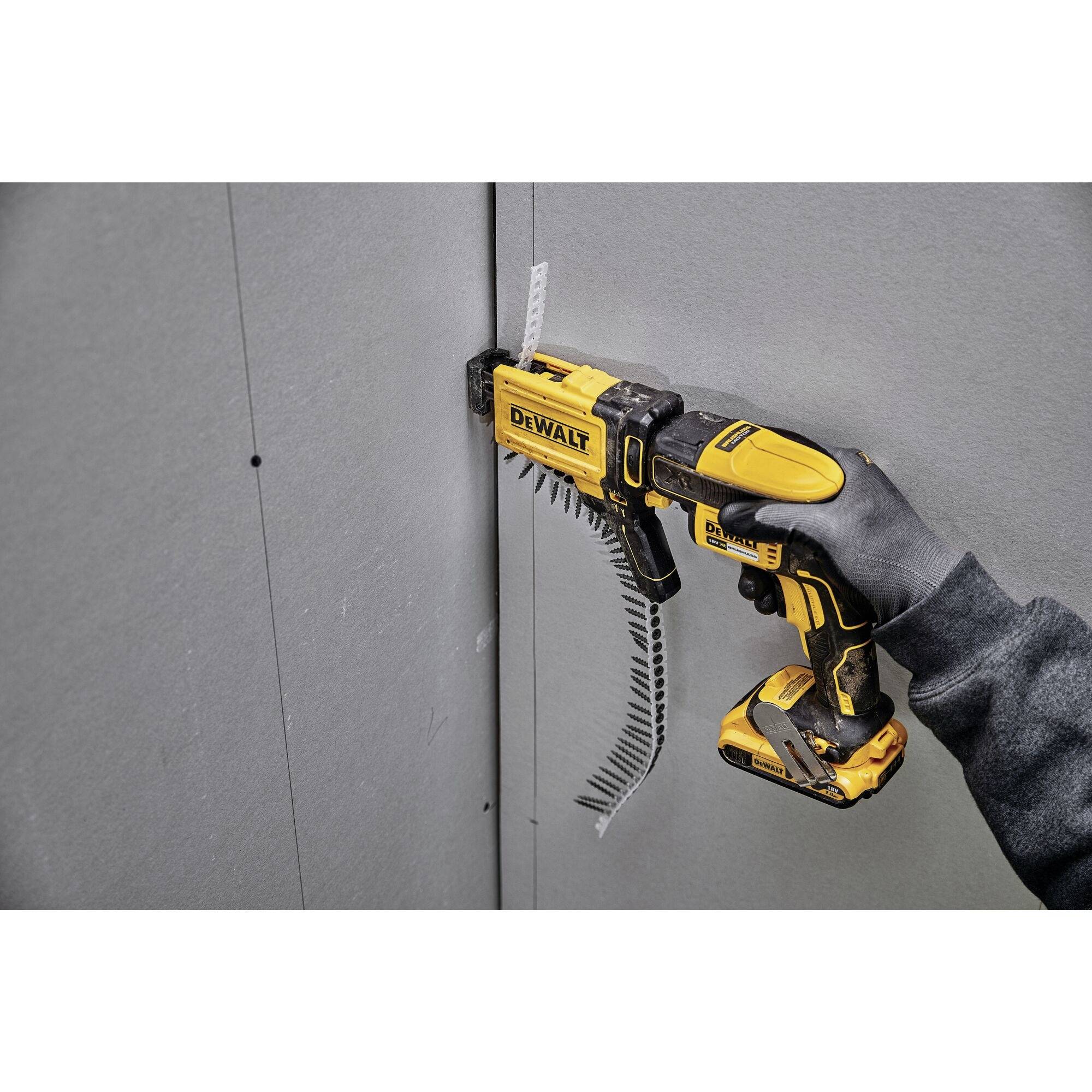 A person is using a yellow power drill to screw a screw into a grey plasterboard wall.