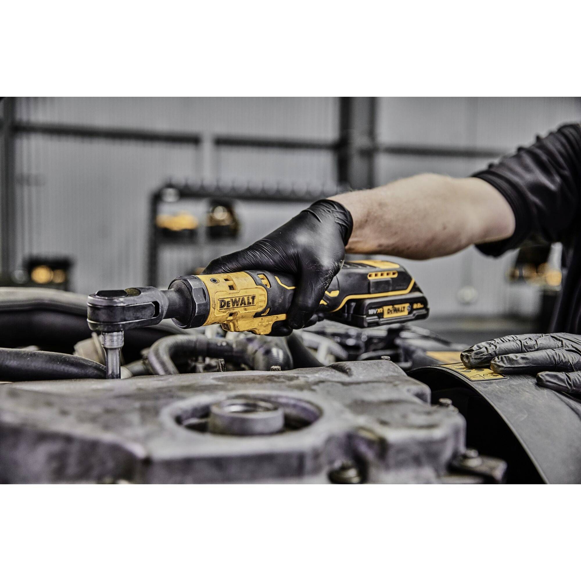 A person is working with a yellow cordless drill in a workshop. They are wearing black gloves and drilling into a metal component.