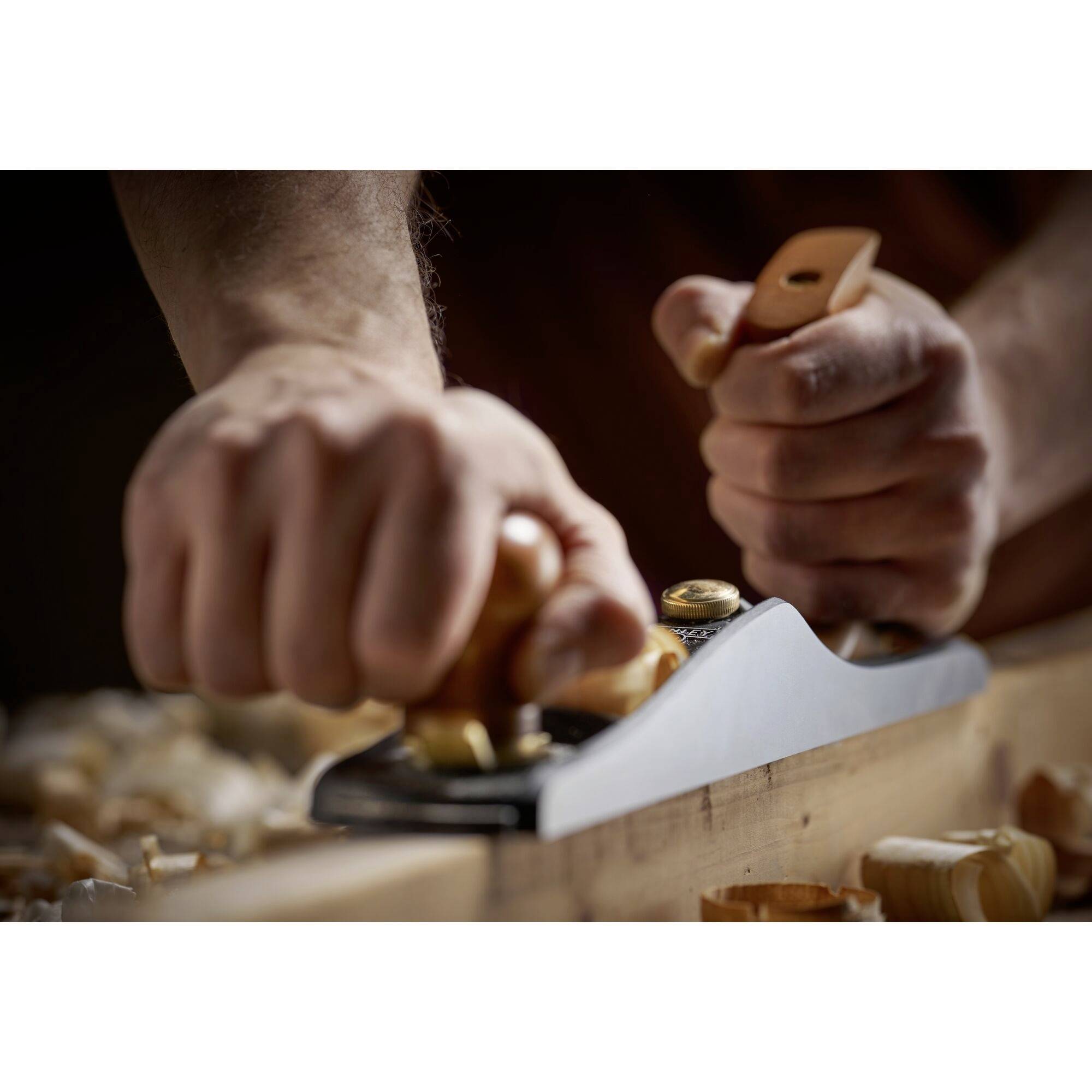 A person is planing a wooden board with a hand planer. Wood shavings are scattered on the table. Focused on the working motion.