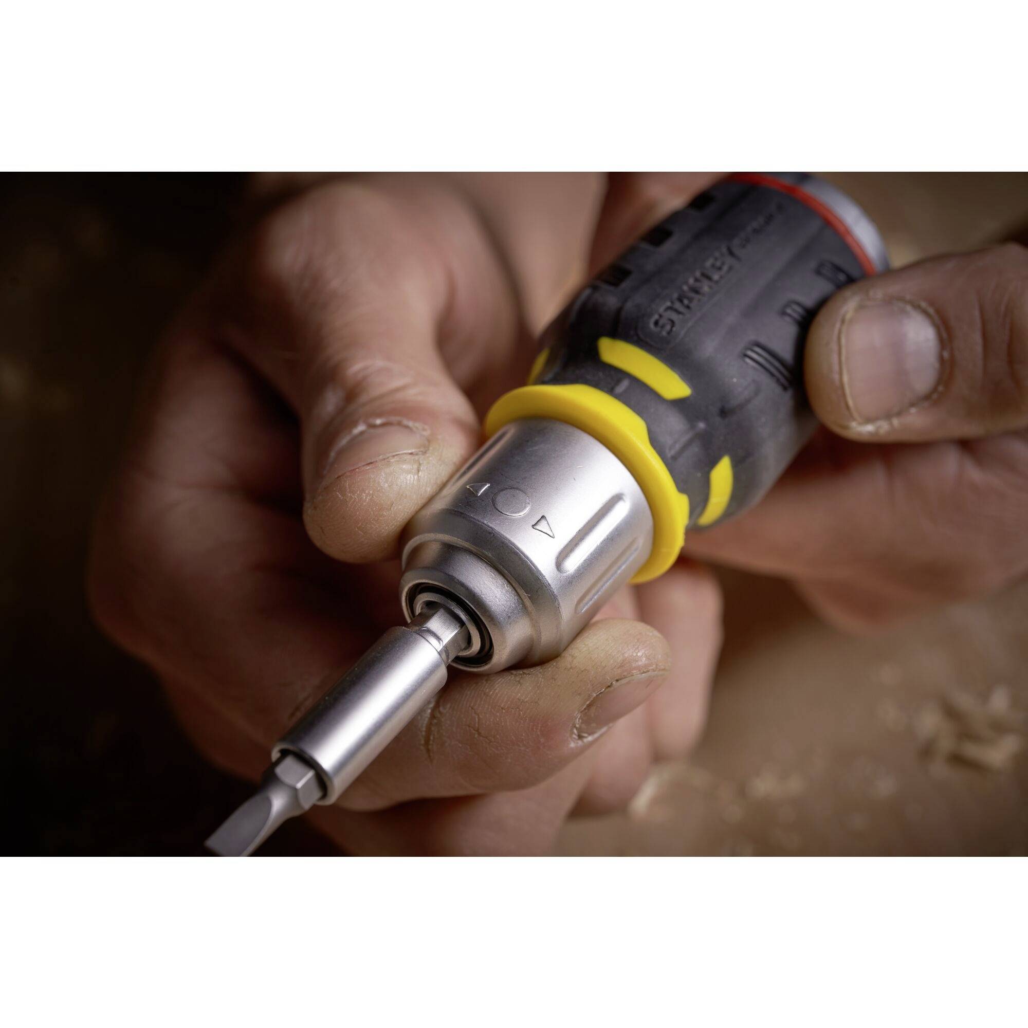 Close-up of a screwdriver with yellow and red accents, being held by a hand. The tip is pointing downwards.