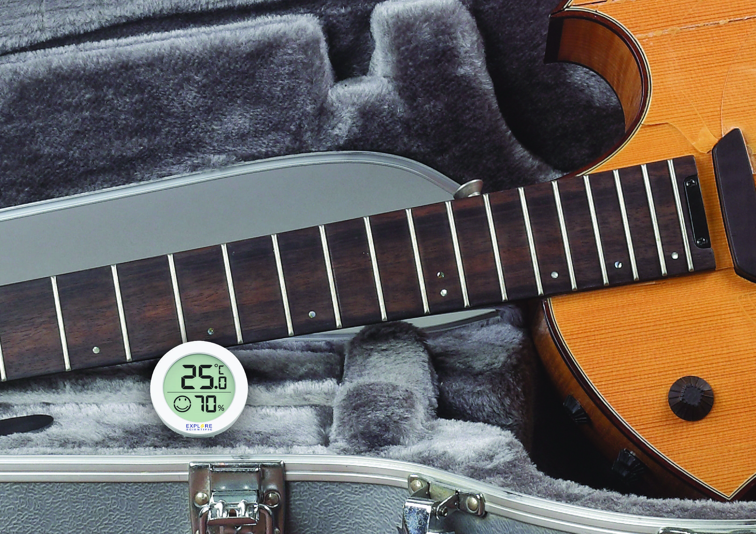 An acoustic guitar lies in an open case lined with velvet. A hygrometer indicates a temperature of 25.6°C and 70% humidity.