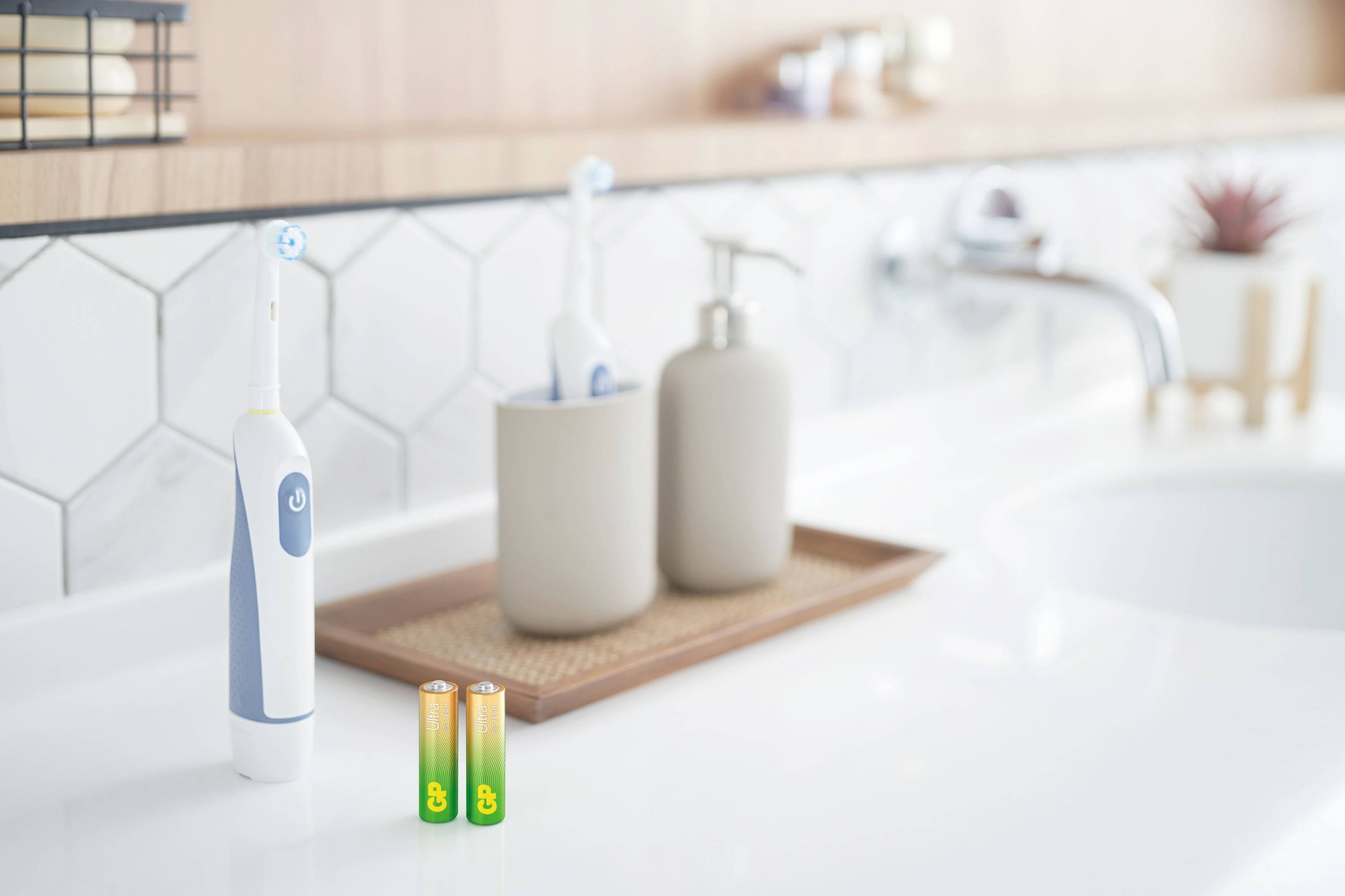 Electric toothbrush next to two AA batteries on a bathroom sink, with a soap dispenser and washbasin beside it.