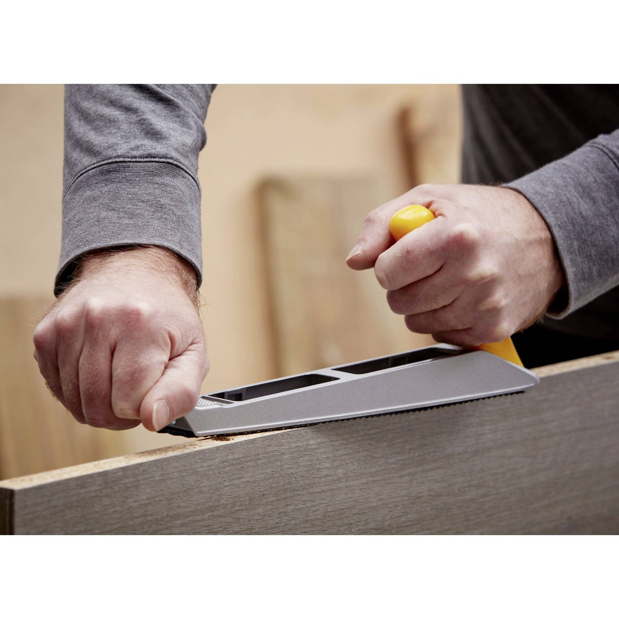 A person is planing a piece of wood with a hand plane. Their hands grip the tool firmly as wood shavings curl away.