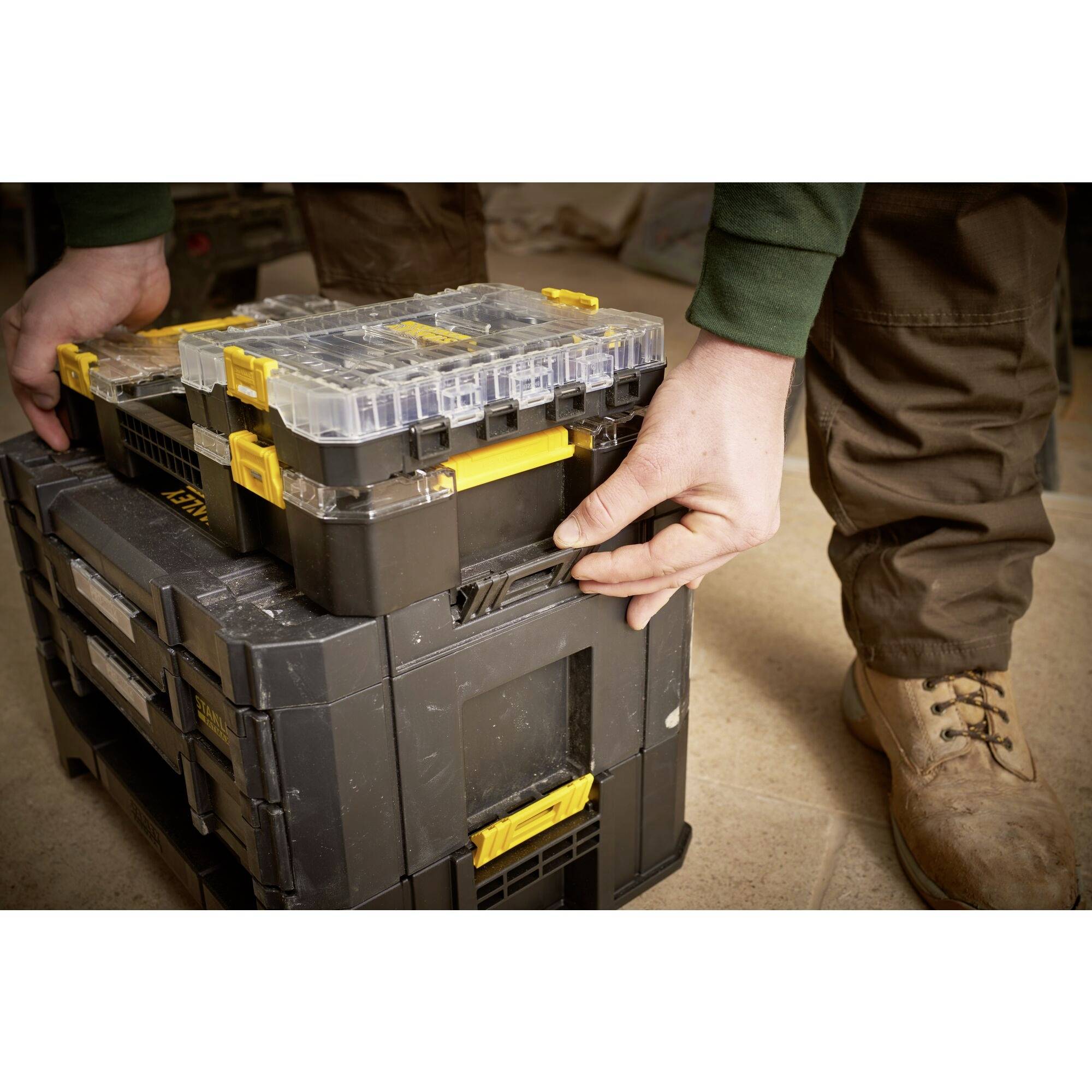 A person is stacking boxes with yellow handles on top of each other, possibly during a manual or construction task.