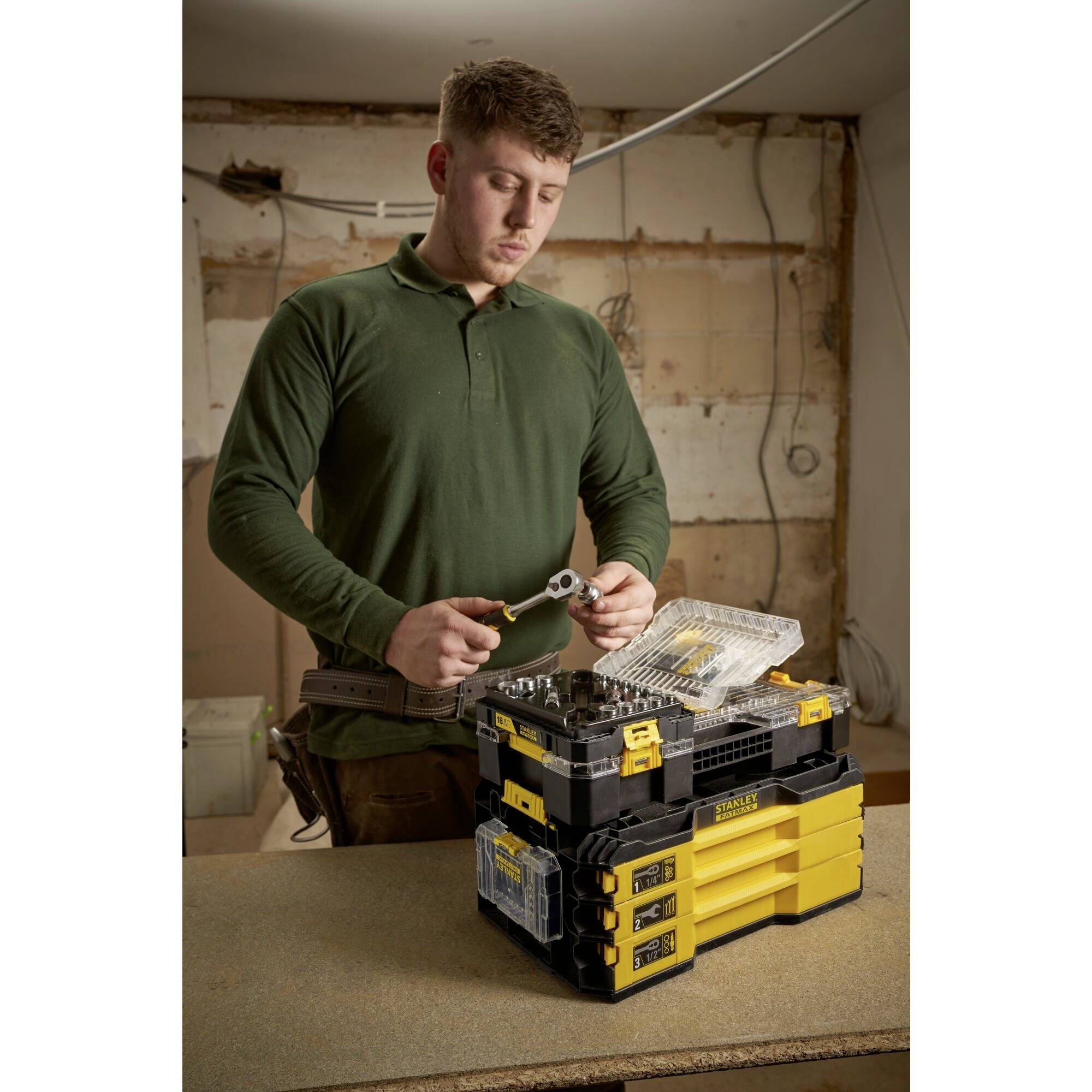 A person is working on a toolbox and holding a tool in a construction site or workshop environment.