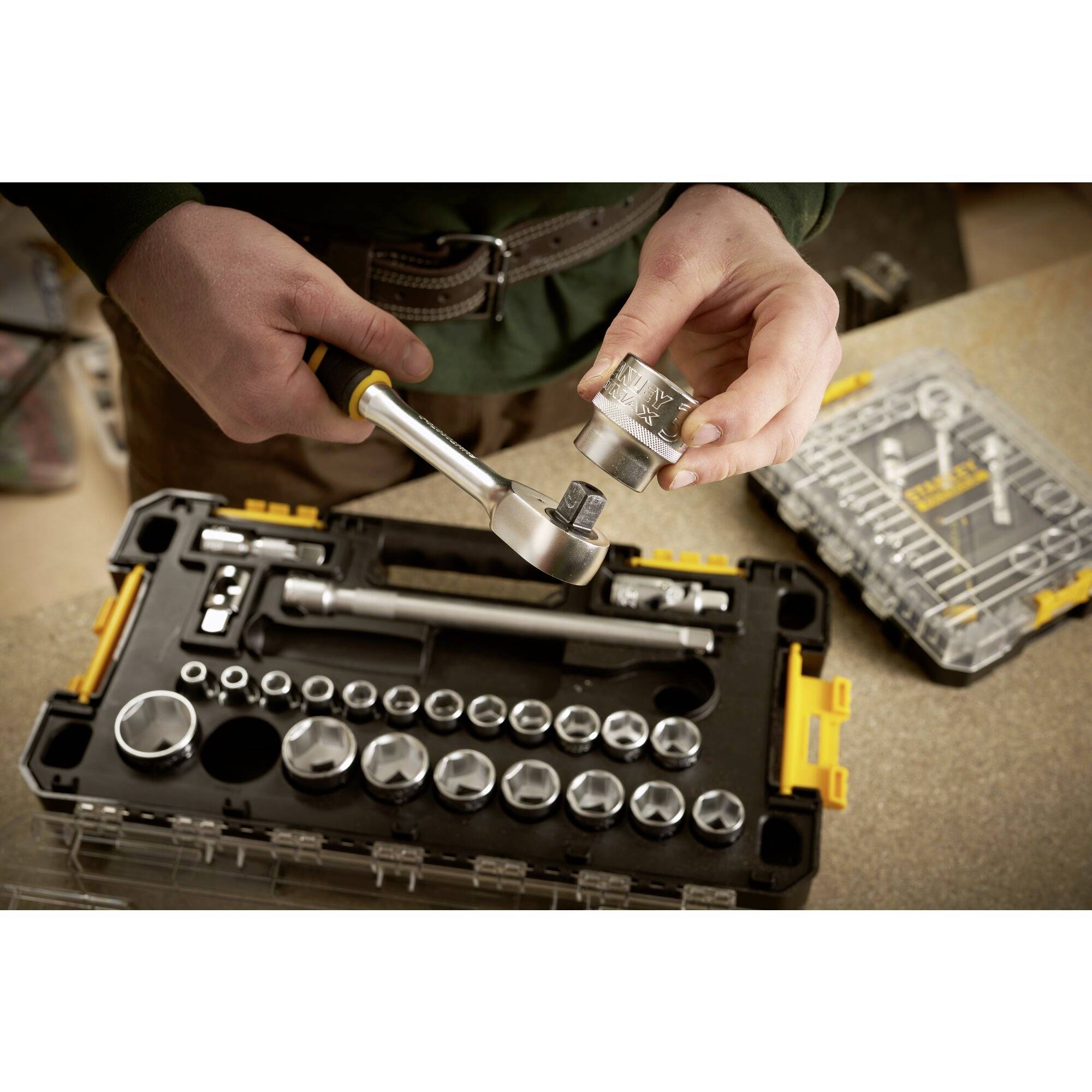 A person is holding a socket wrench and a nut over an open toolbox with various sizes of socket attachments.