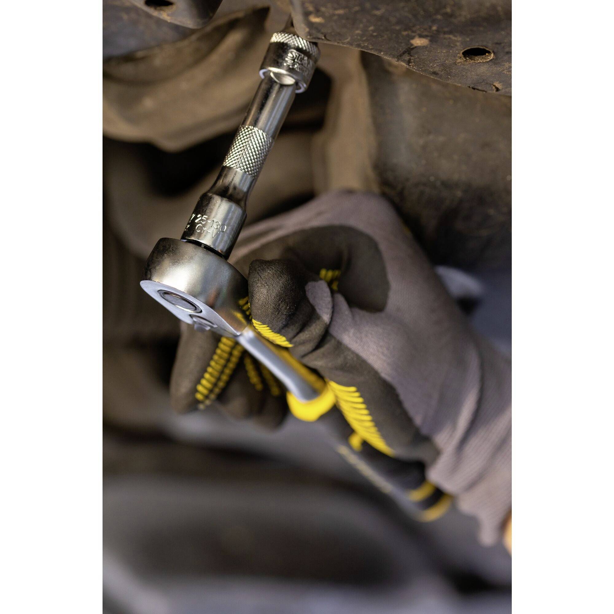 A person wearing gloves is using a socket wrench to tighten a screw on a vehicle part.