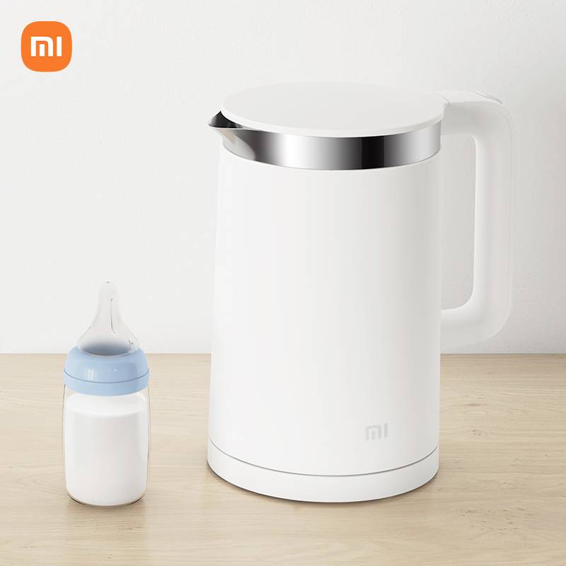 A white kettle and a baby bottle are placed side by side on a wooden table. The kettle bears the logo of an electronics brand.
