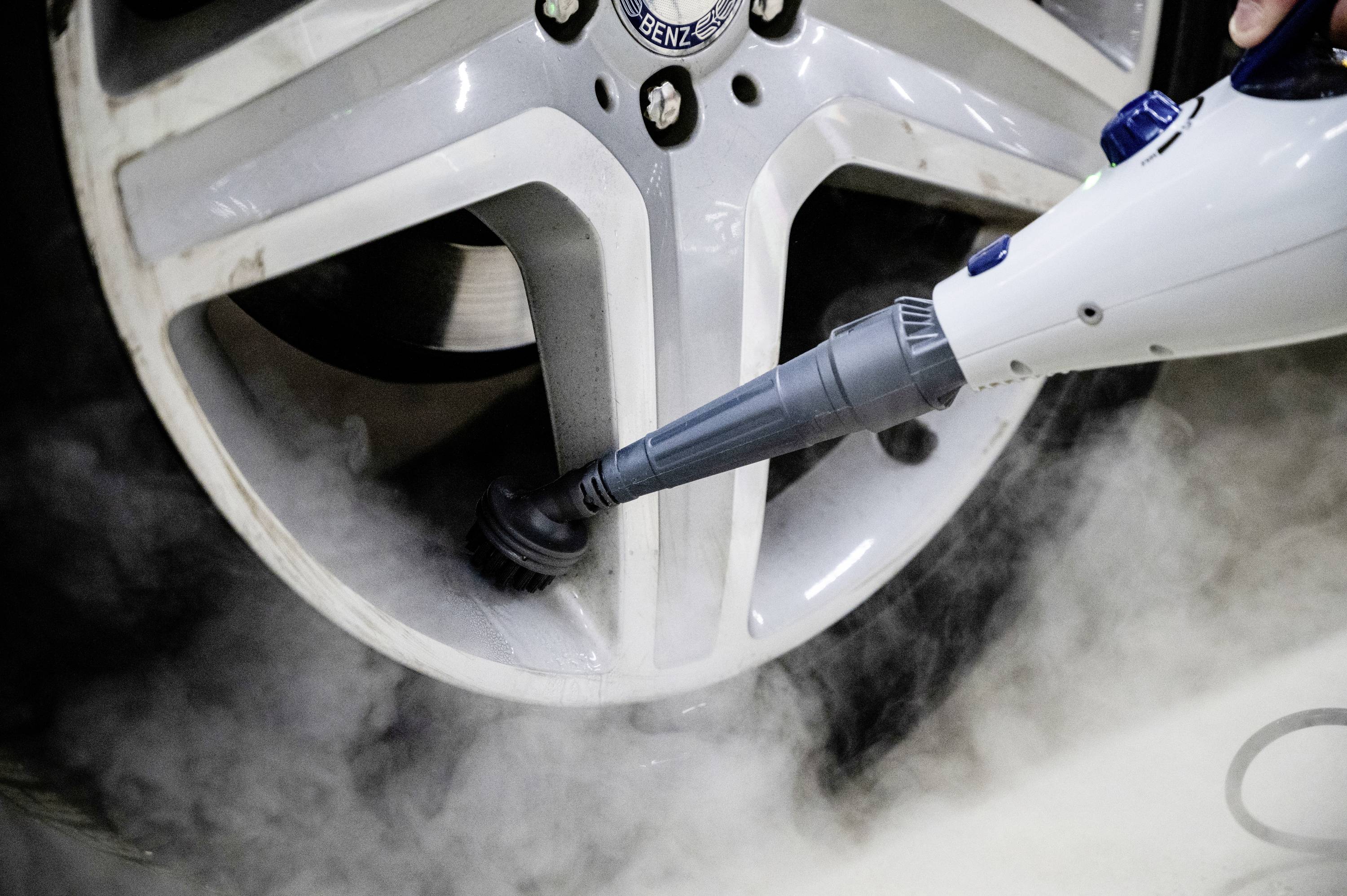 A steam cleaner removes dirt from a silver car wheel.