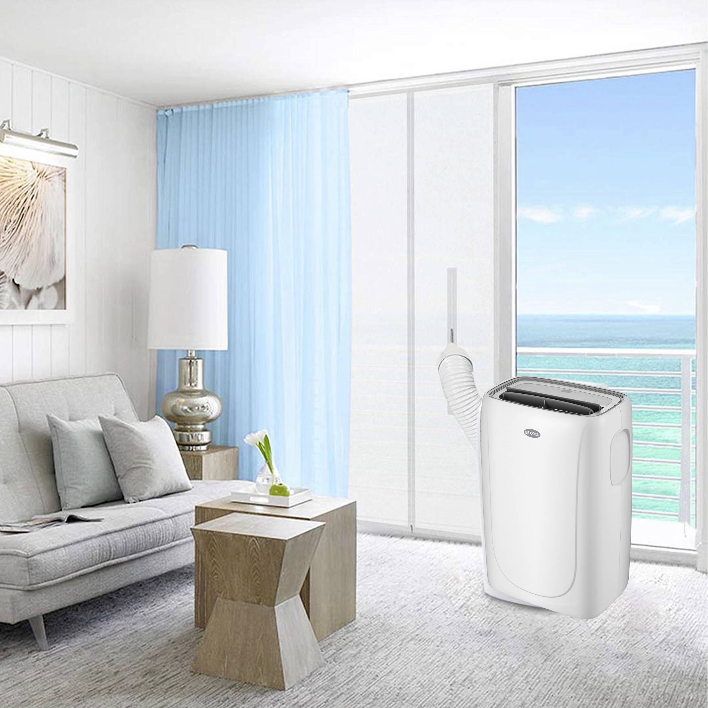 A portable air conditioning unit stands in a bright living room with a view of the sea. A large window frontage allows plenty of light to enter.