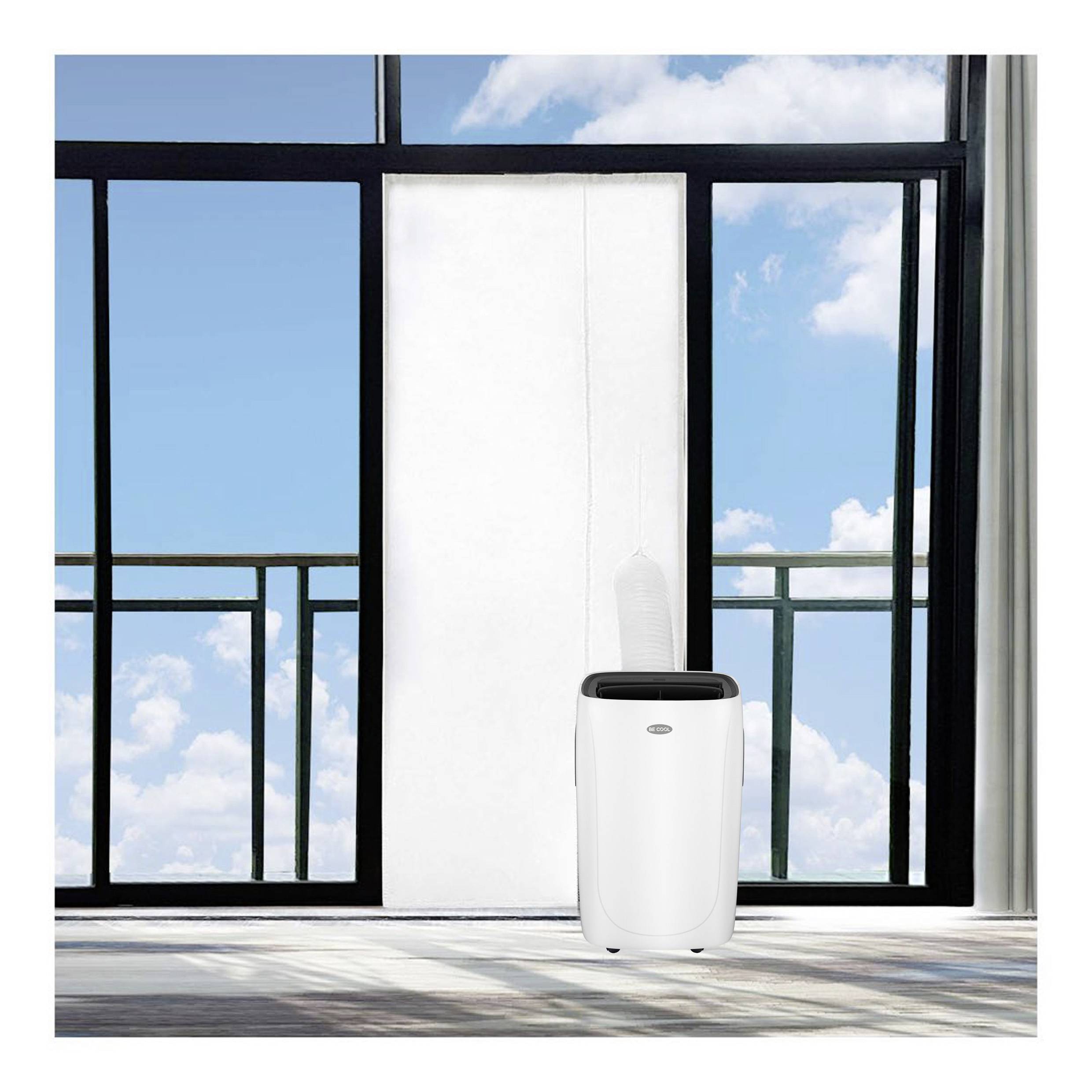 A portable air conditioning unit stands in front of a large glass door, through which blue sky and clouds are visible.