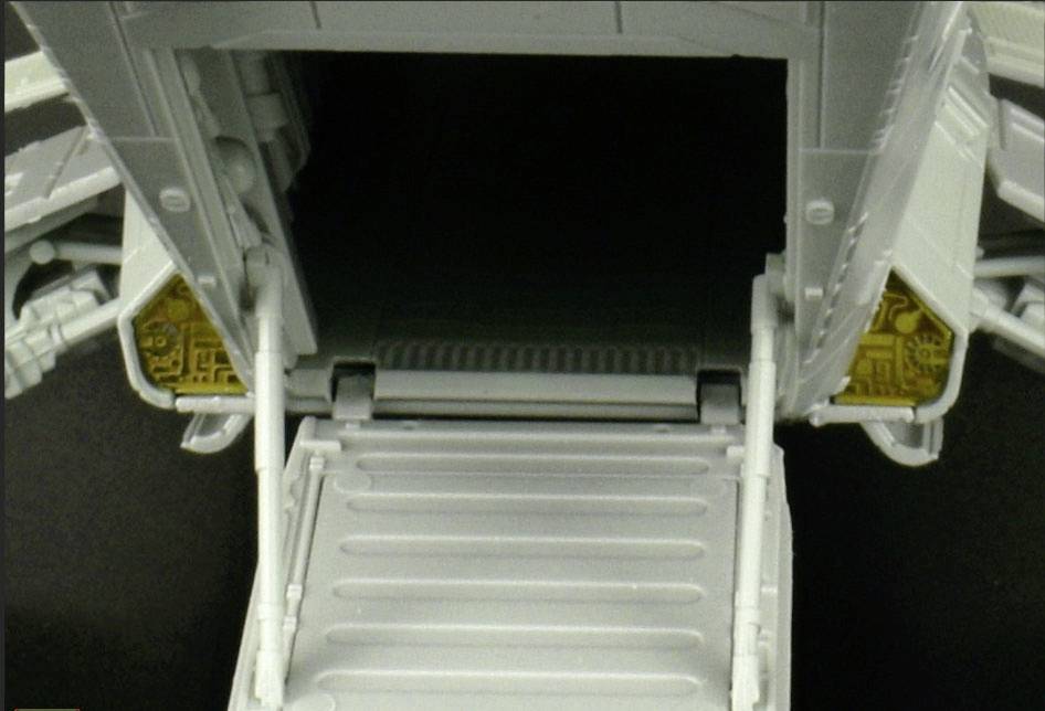 A grey loading bay leading into a dark room, surrounded by technical details at the edges.