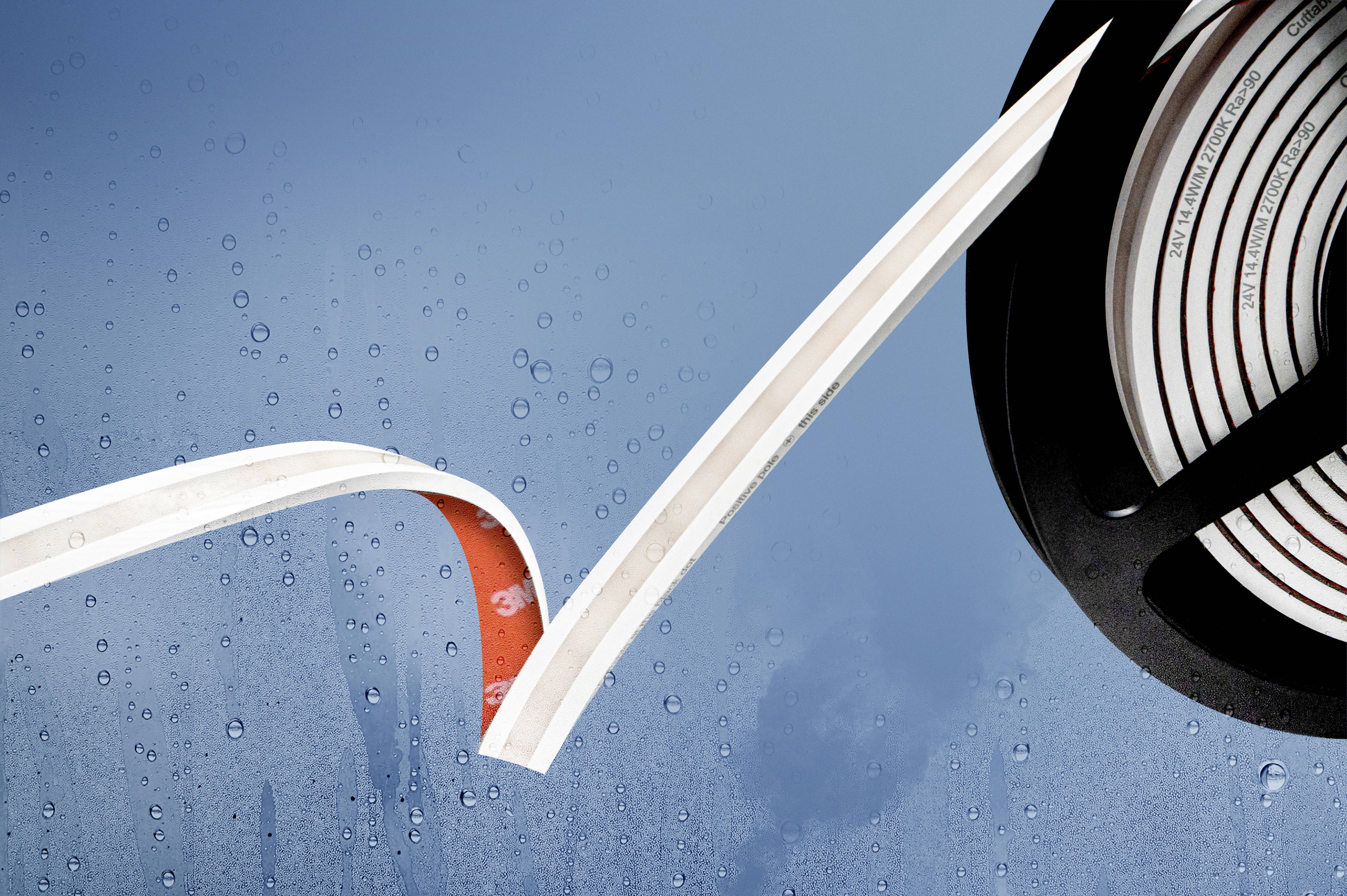 A roll of adhesive tape, partially unpeeled, in front of a rain-soaked window. The tape has a white and a red side.