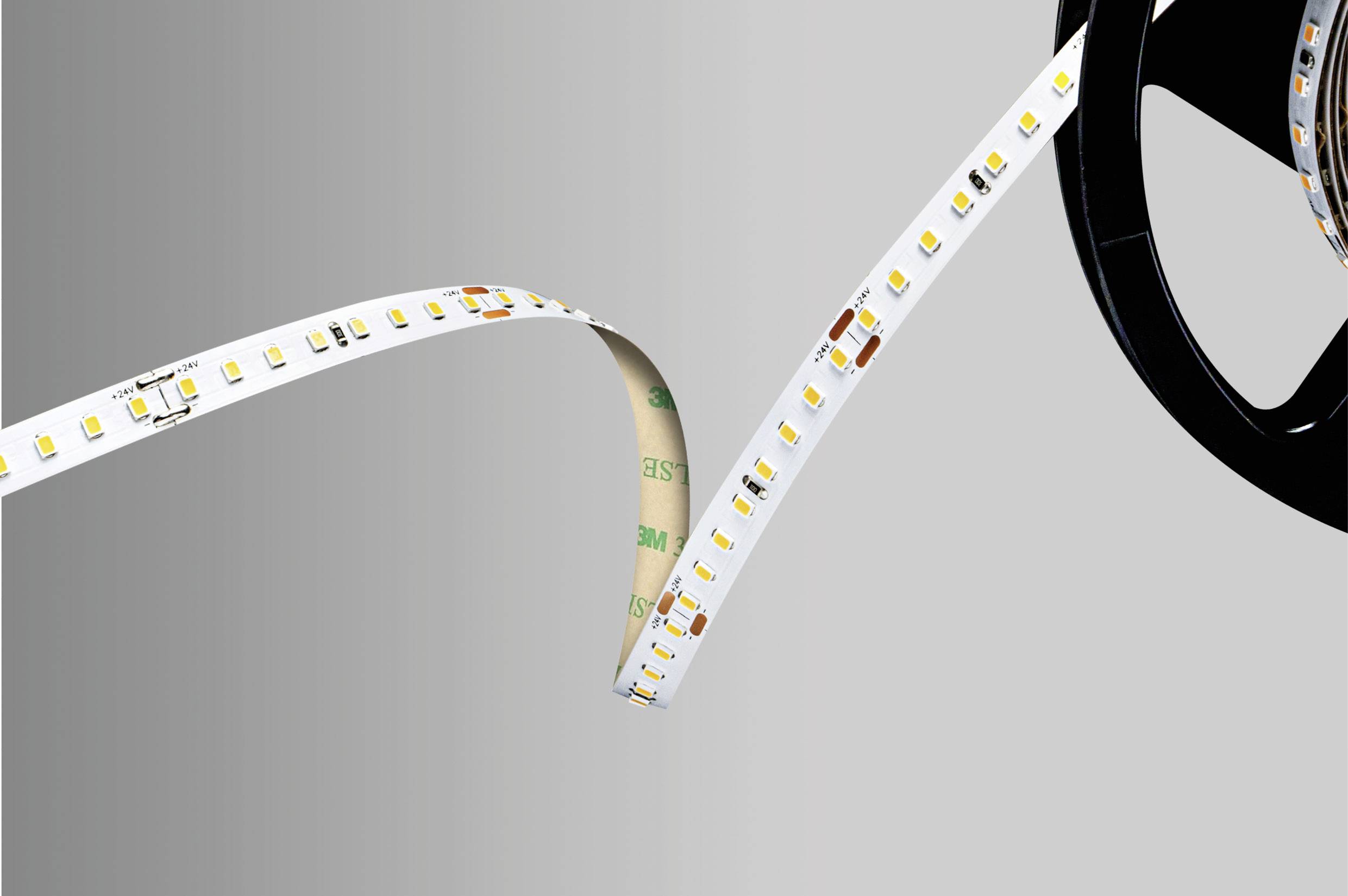 A LED strip, partially unrolled from a reel, shown against a grey background. Ideal for lighting purposes.