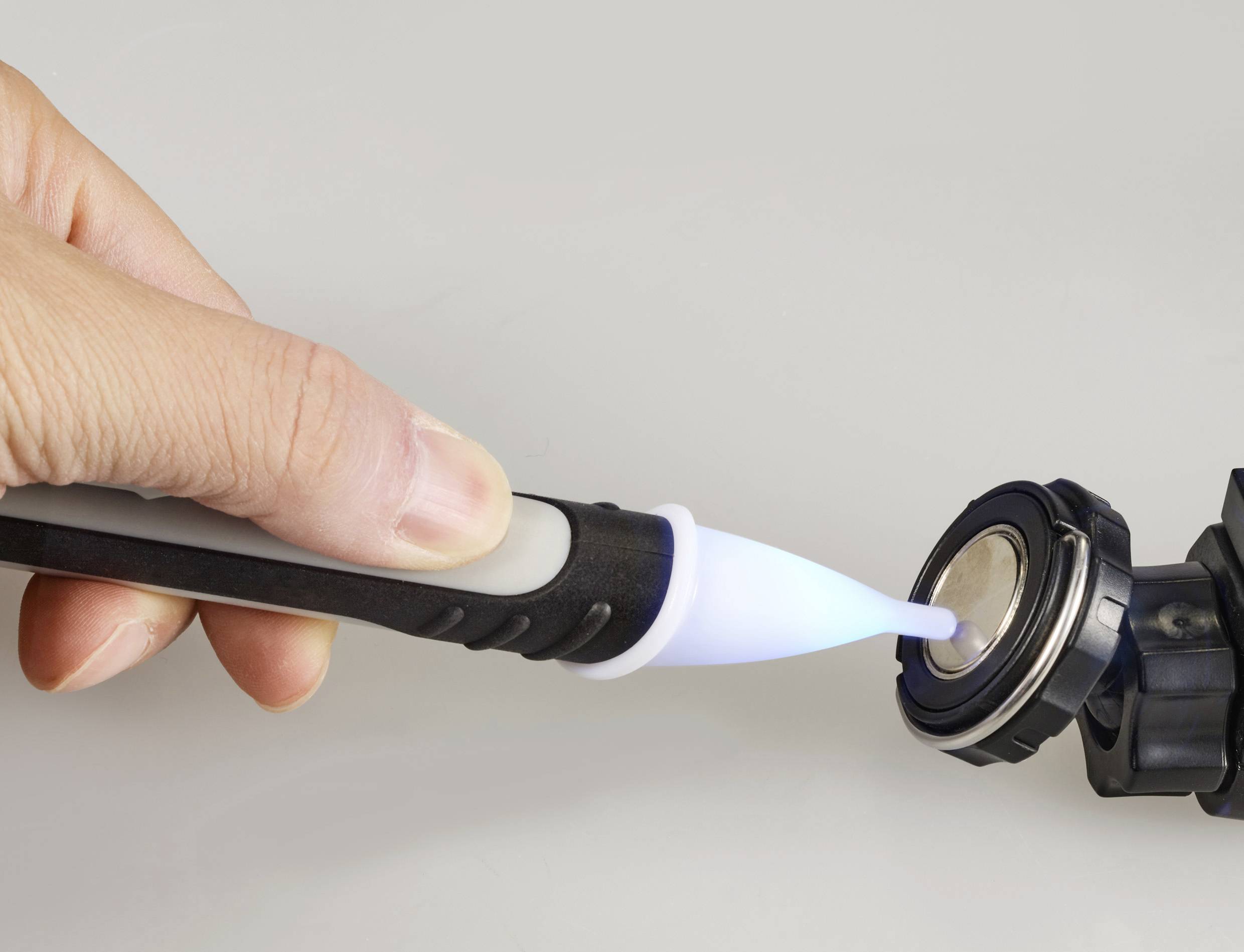 A hand holds an ultraviolet light pen, which is directed at a small round metal object in order to cure or repair it.
