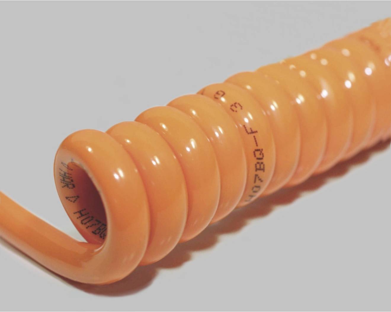 An orange, spiral-shaped cable lies on a grey background.