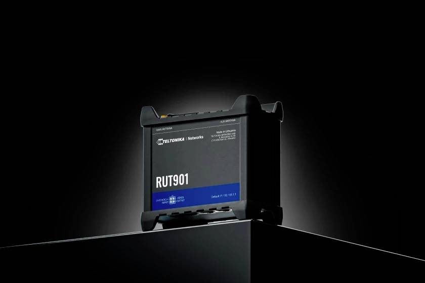 A black telecommunications device with the inscription 'RUT901' stands on a plinth. The background is dark, emphasising the device.
