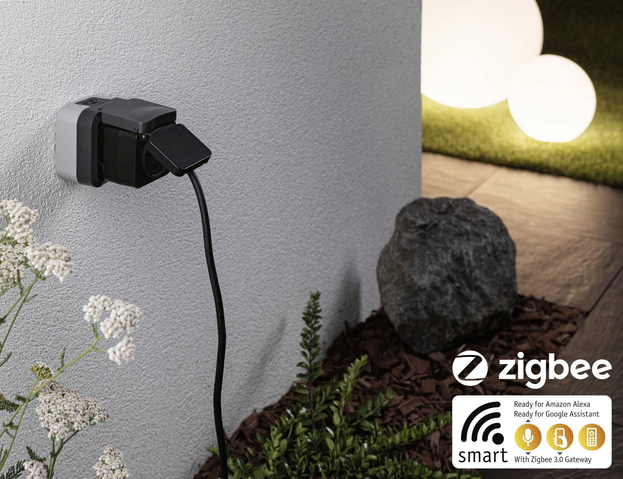 An outdoor power socket with a connected device cable. 'Zigbee' logo in the bottom right, indicating compatibility with Alexa and Google Assistant.