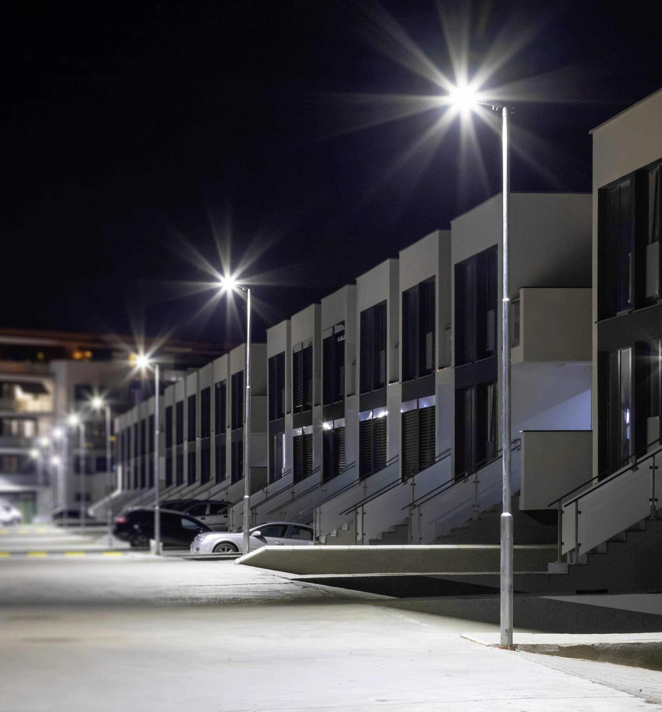 Row of modern terraced houses at night, illuminated by bright street lamps. Several cars are parked along the street.