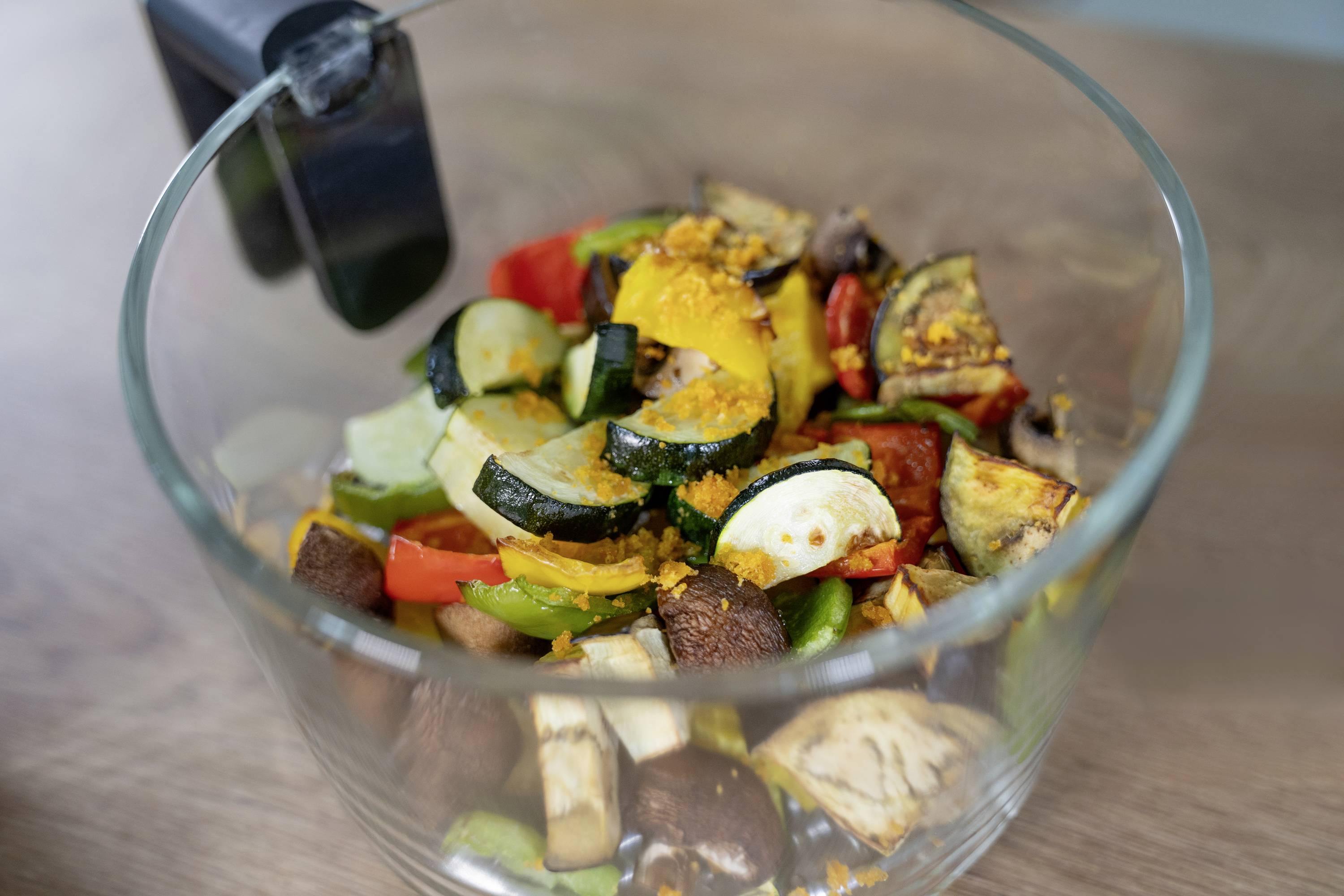 A glass bowl filled with freshly chopped vegetables such as courgettes, peppers and mushrooms on a wooden table.