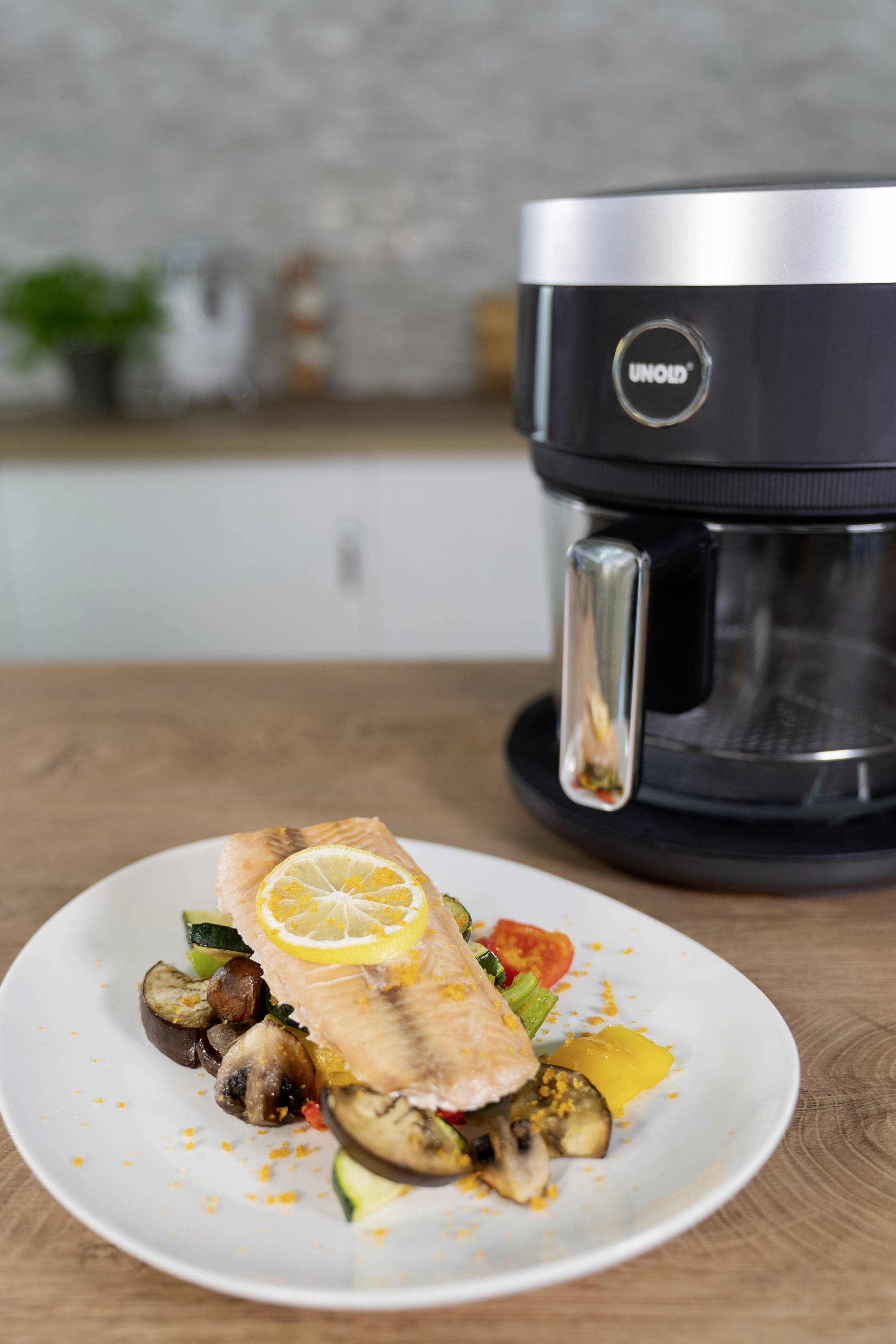 A plate with grilled salmon fillet on vegetables. In the background, a black food processor sits on a worktop.