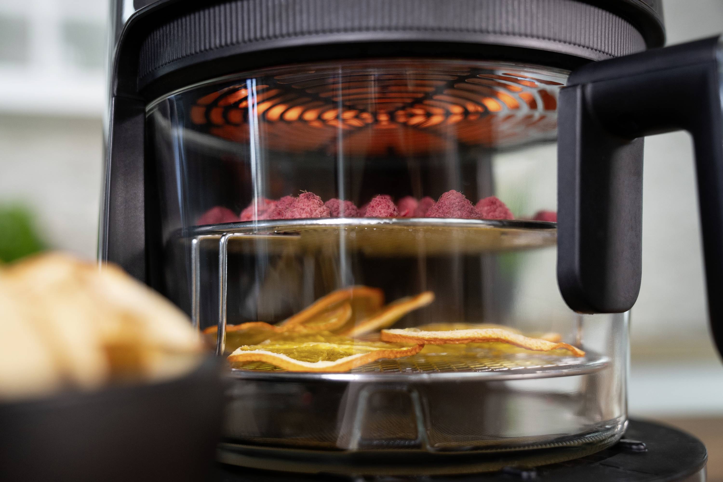 A food dehydrator dries red and orange fruit slices. A fan ensures even heat distribution.