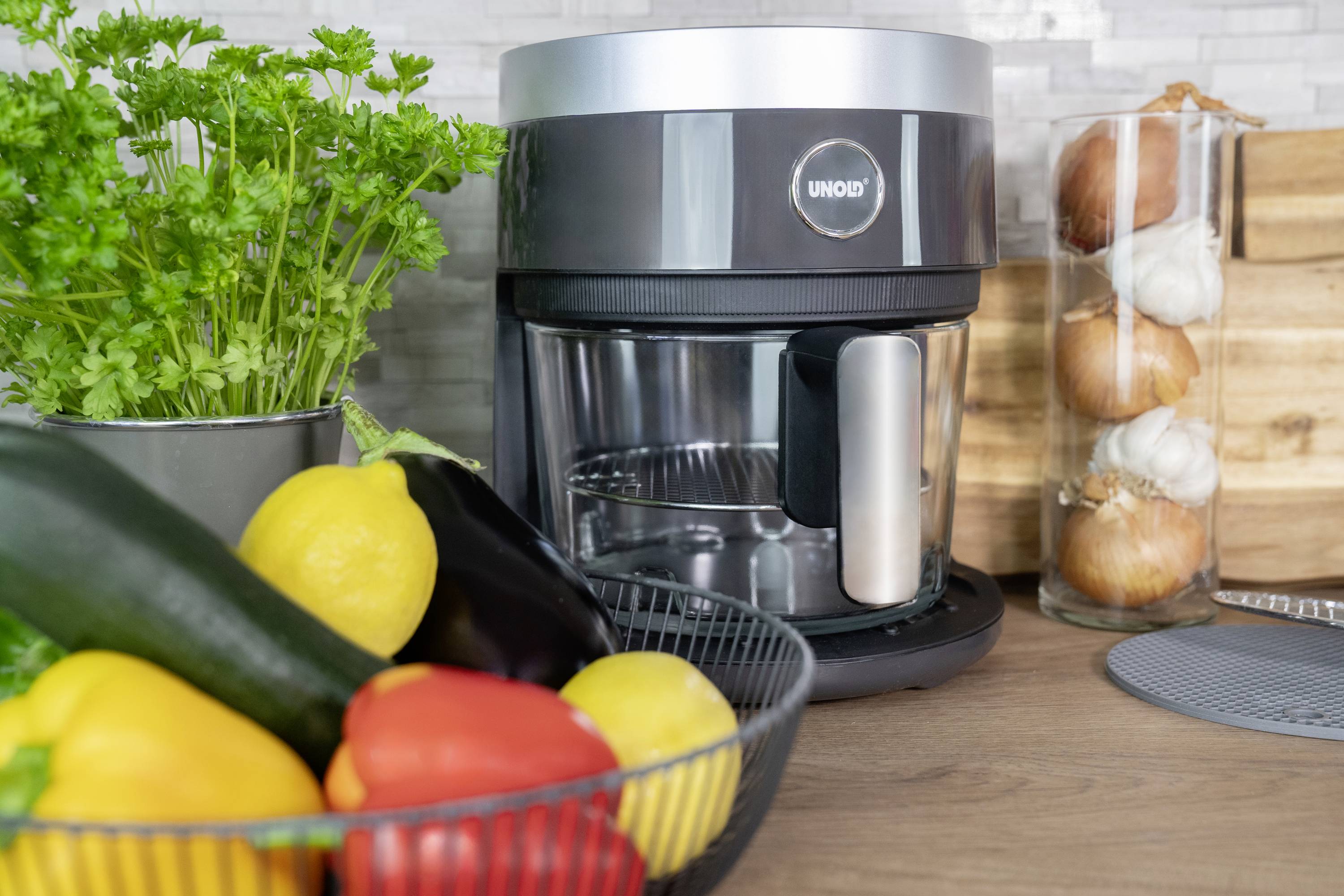 Food processor on the worktop next to a vegetable basket with peppers and courgettes and a pot of fresh herbs.