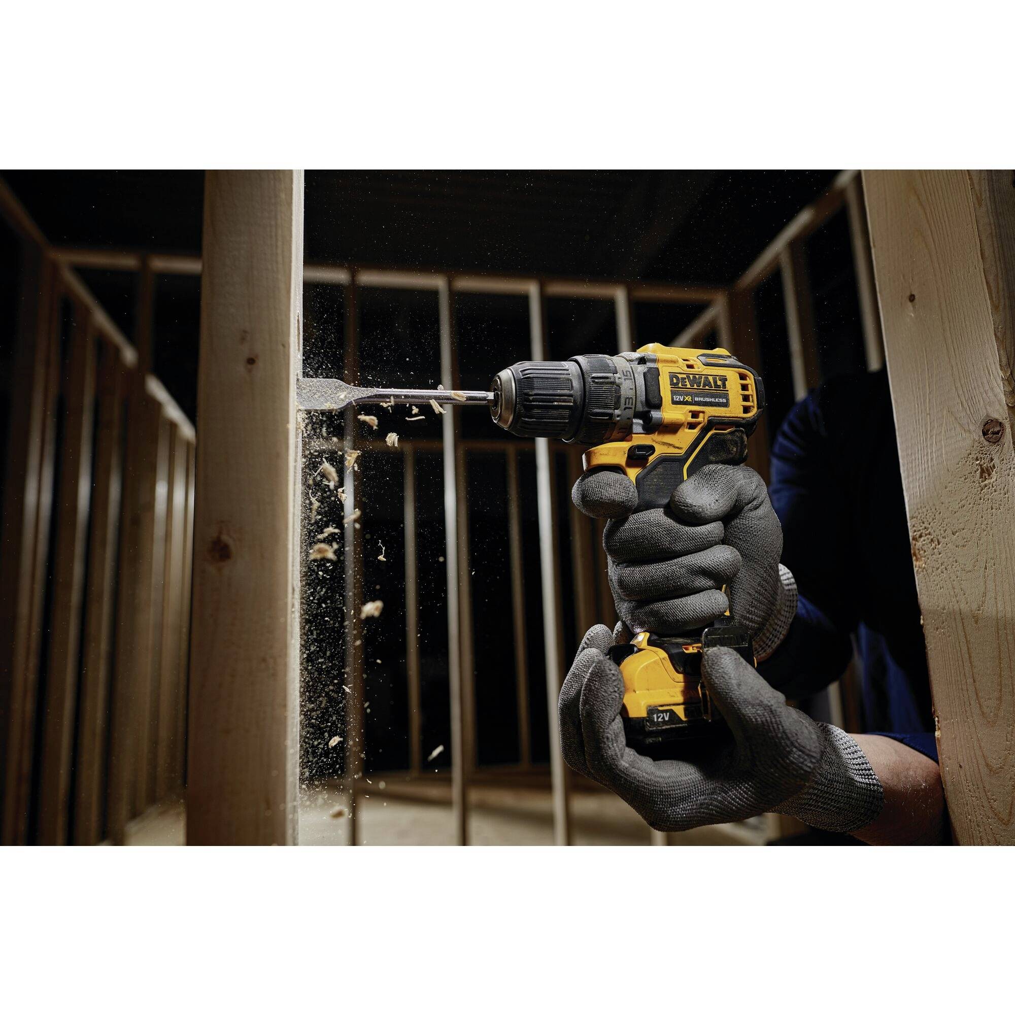 A person is drilling with a yellow cordless drill into a wooden frame, with wood shavings flying. The wooden frame symbolises construction work.