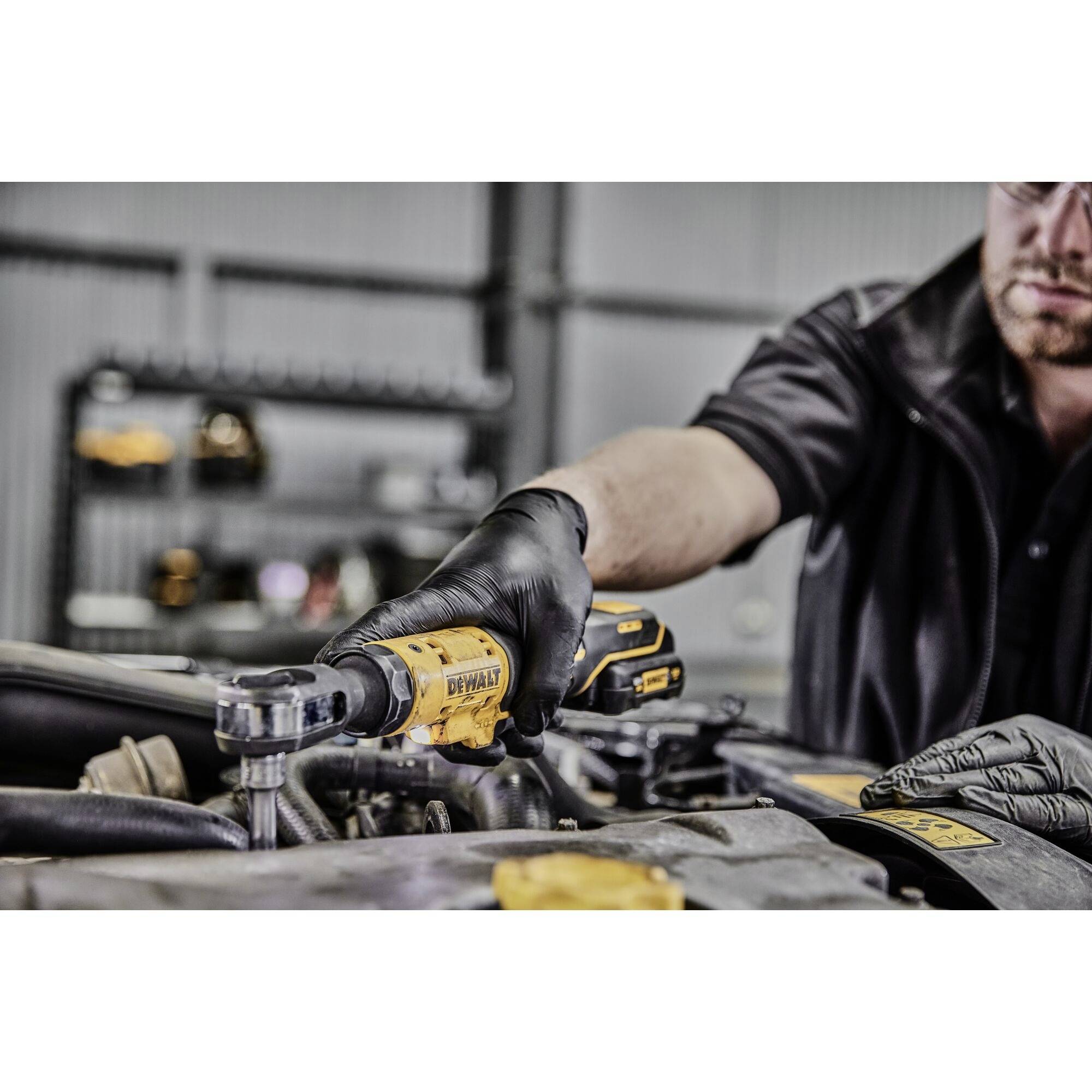 A mechanic in black clothing is using a yellow electrical tool to work on an engine in a workshop.