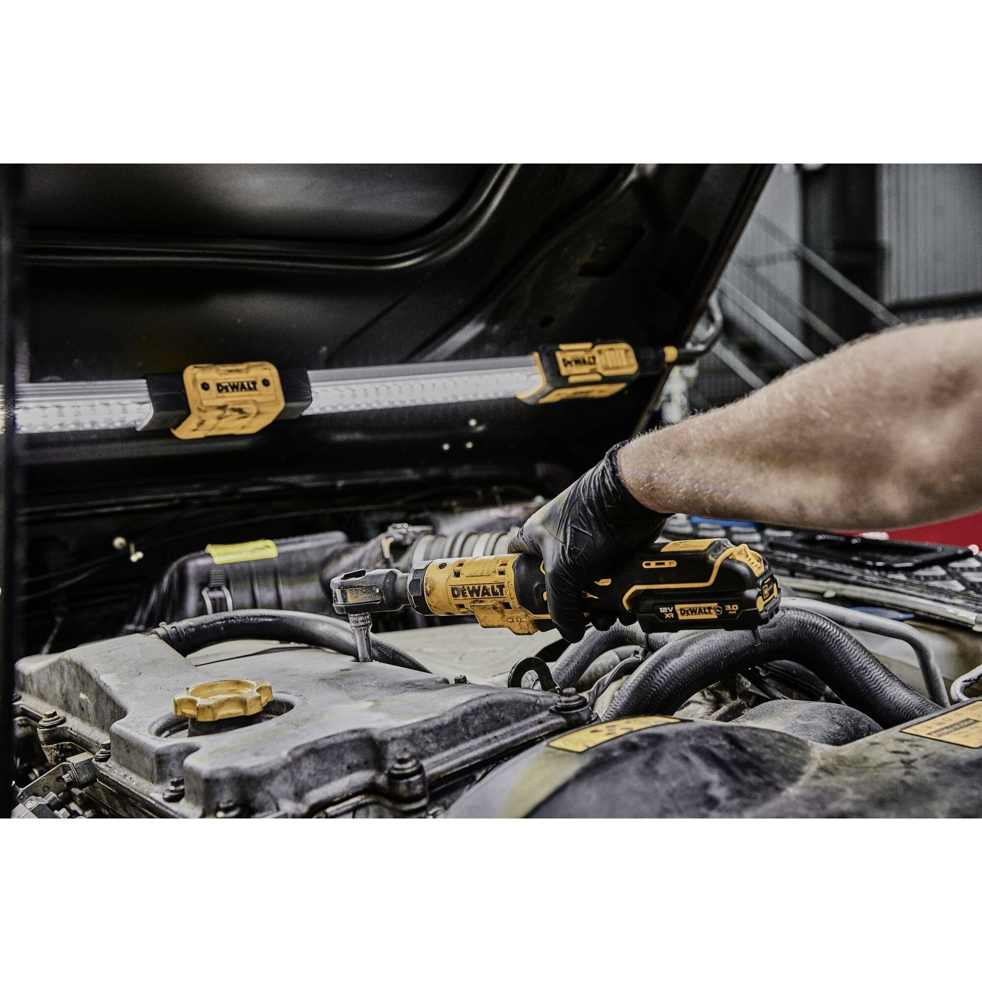 A person is repairing a car's engine using a cordless tool. The focus is on the precise handling of the tool.