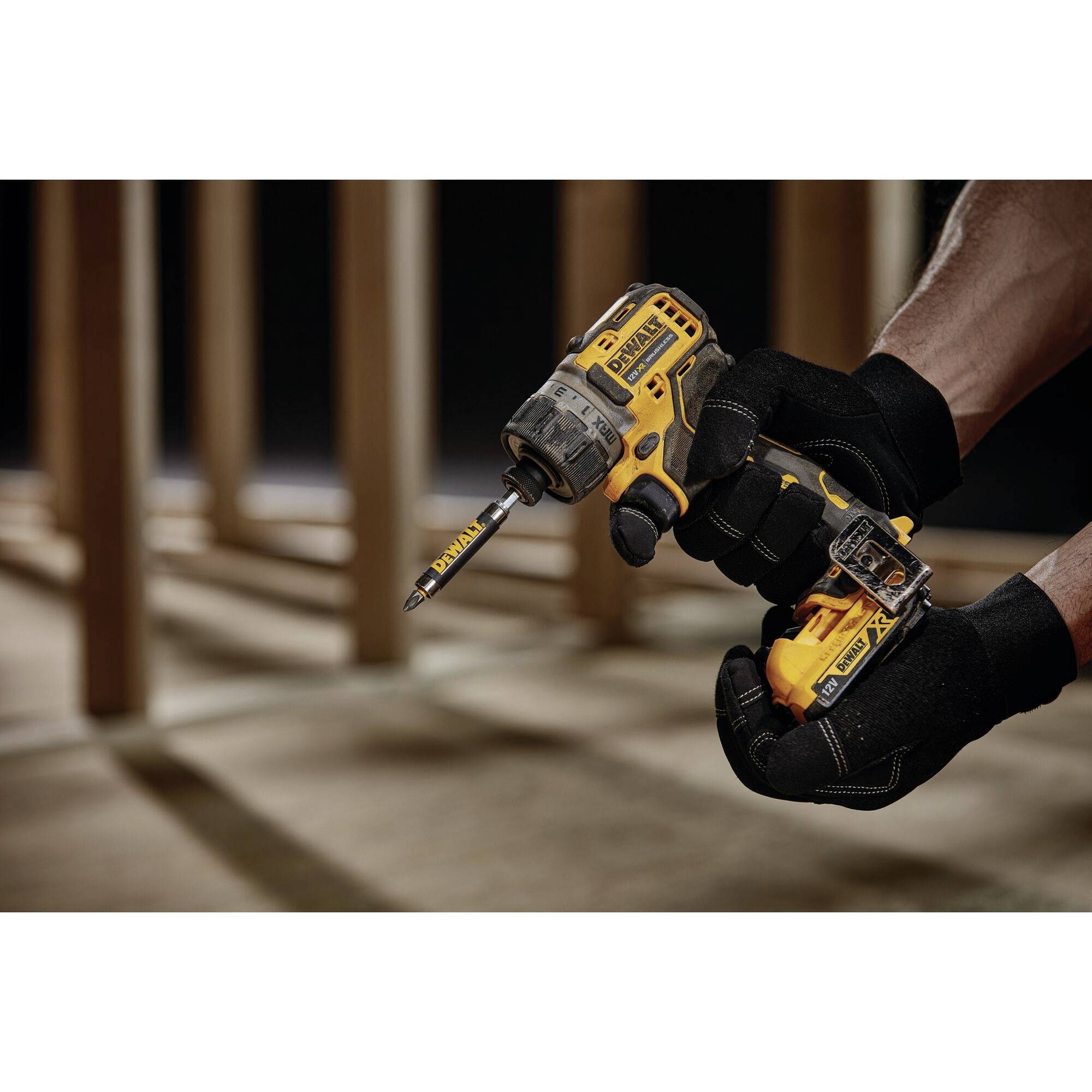 A hand is holding a yellow, cordless drill driver in a room with wooden beams in the background.