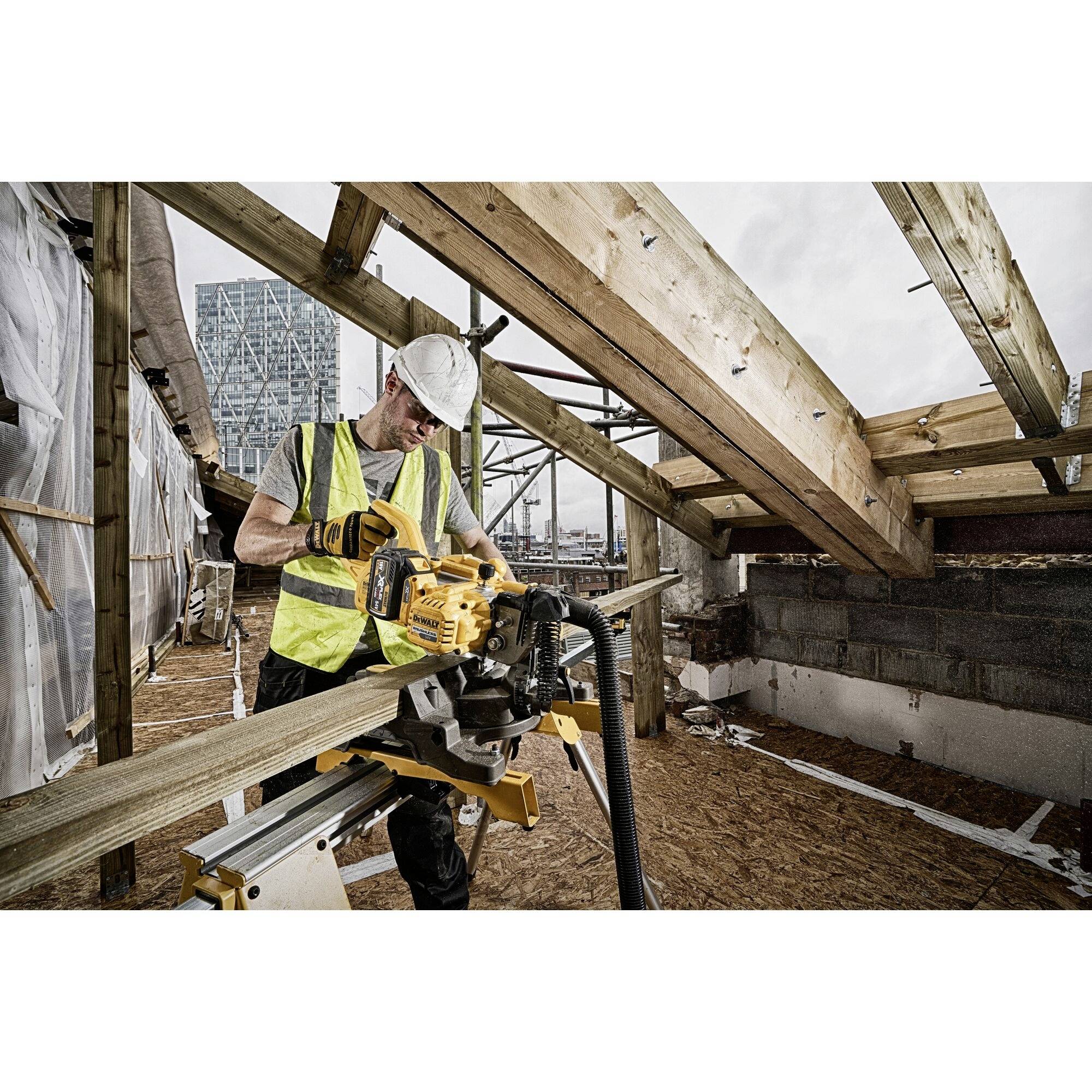 A construction worker is wearing a white hard hat and a yellow high-visibility vest while cutting wood with a saw on a building site.