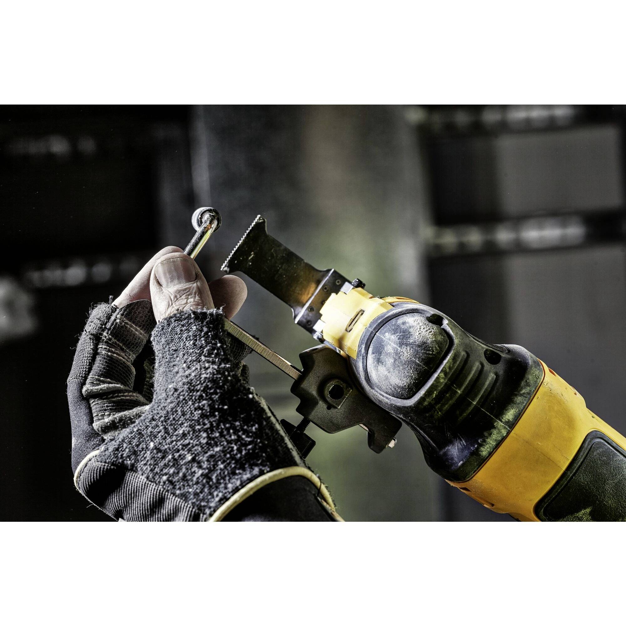 A person is holding a compact electric saw, cutting metal in a workshop. Background is blurred, with focus on the working hand.