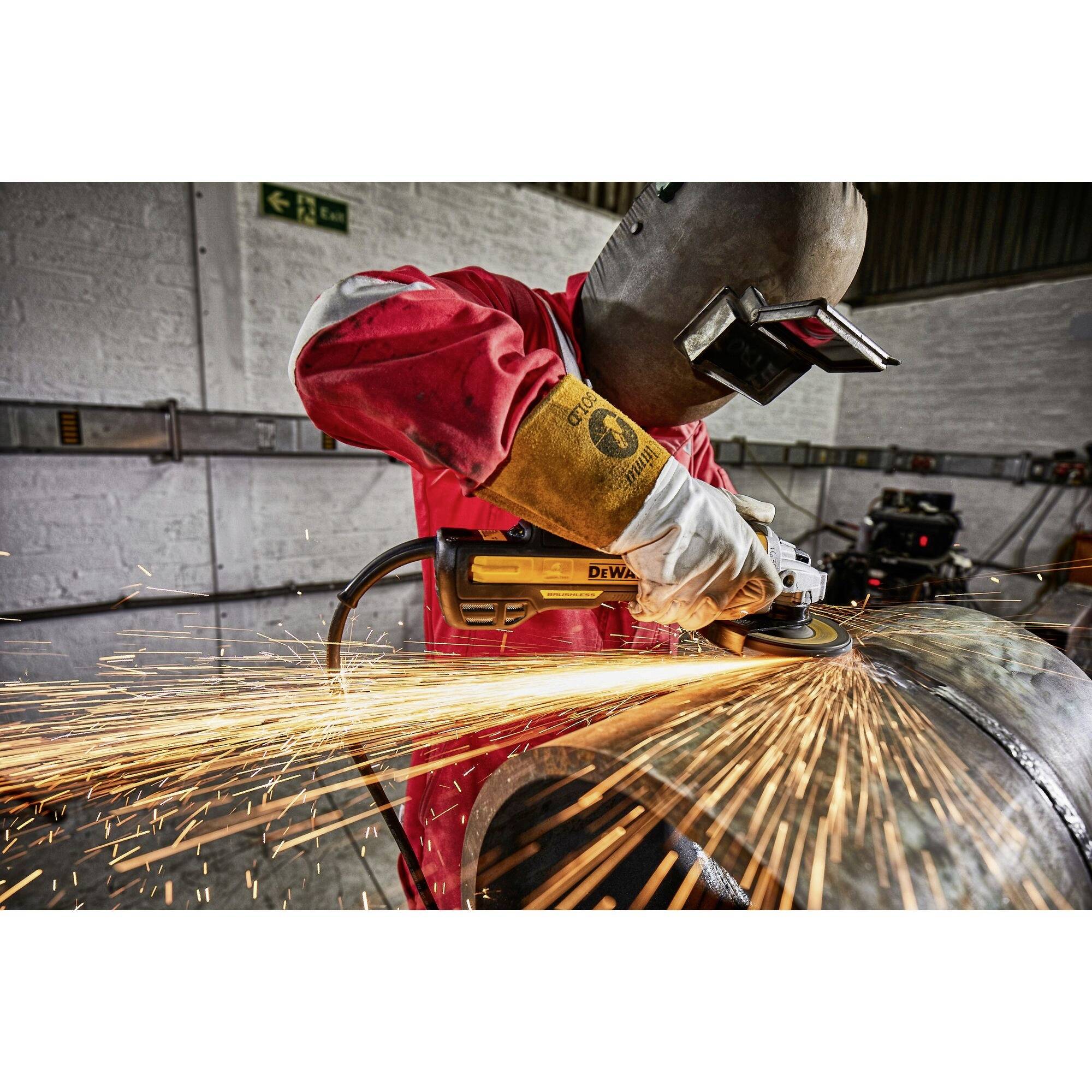 A worker wearing a hard hat is grinding a metal pipe. Sparks are flying, safety equipment is being used. Working environment in a workshop.