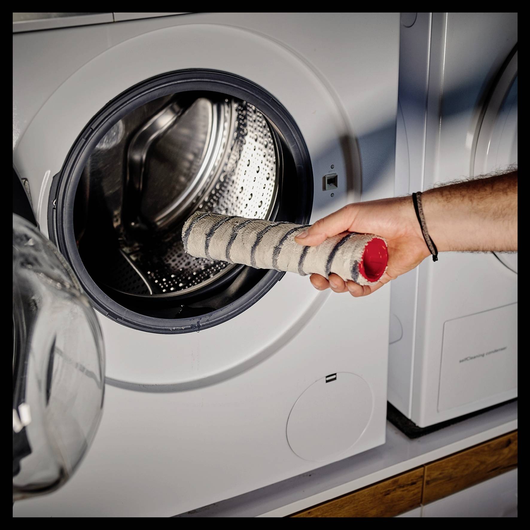 Someone is cleaning the washing machine by holding the lint filter in one hand to check it.