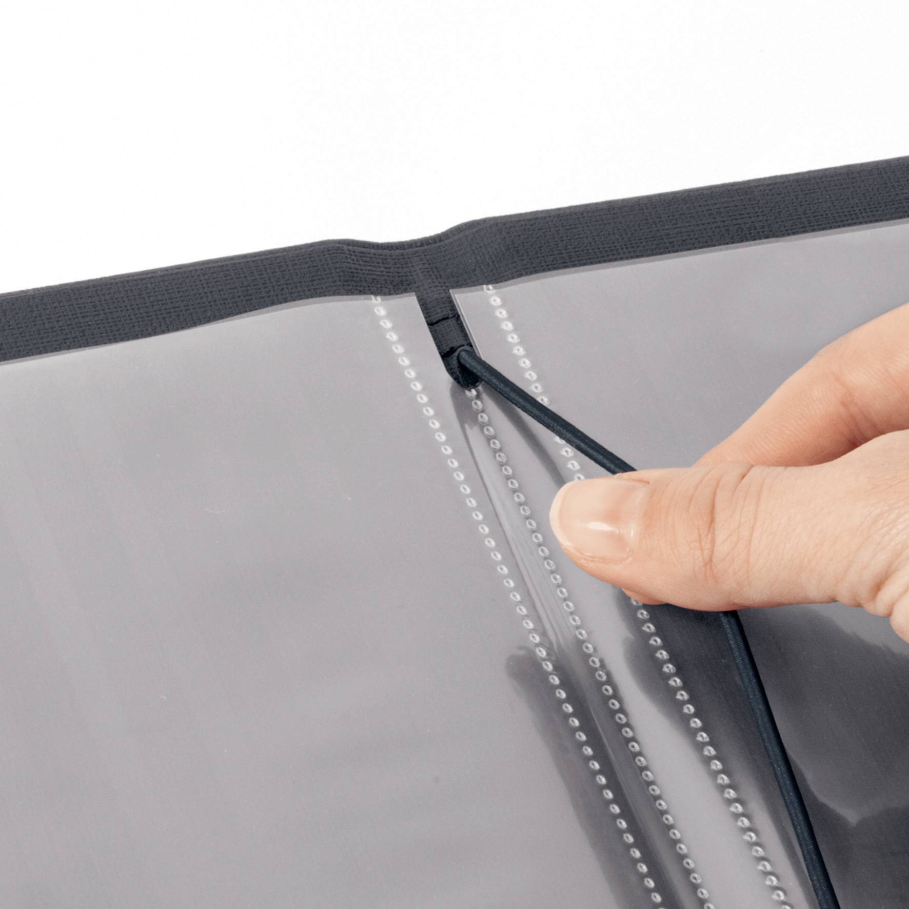 A hand pulls on the elastic band closure of a black ring binder with transparent sleeves.