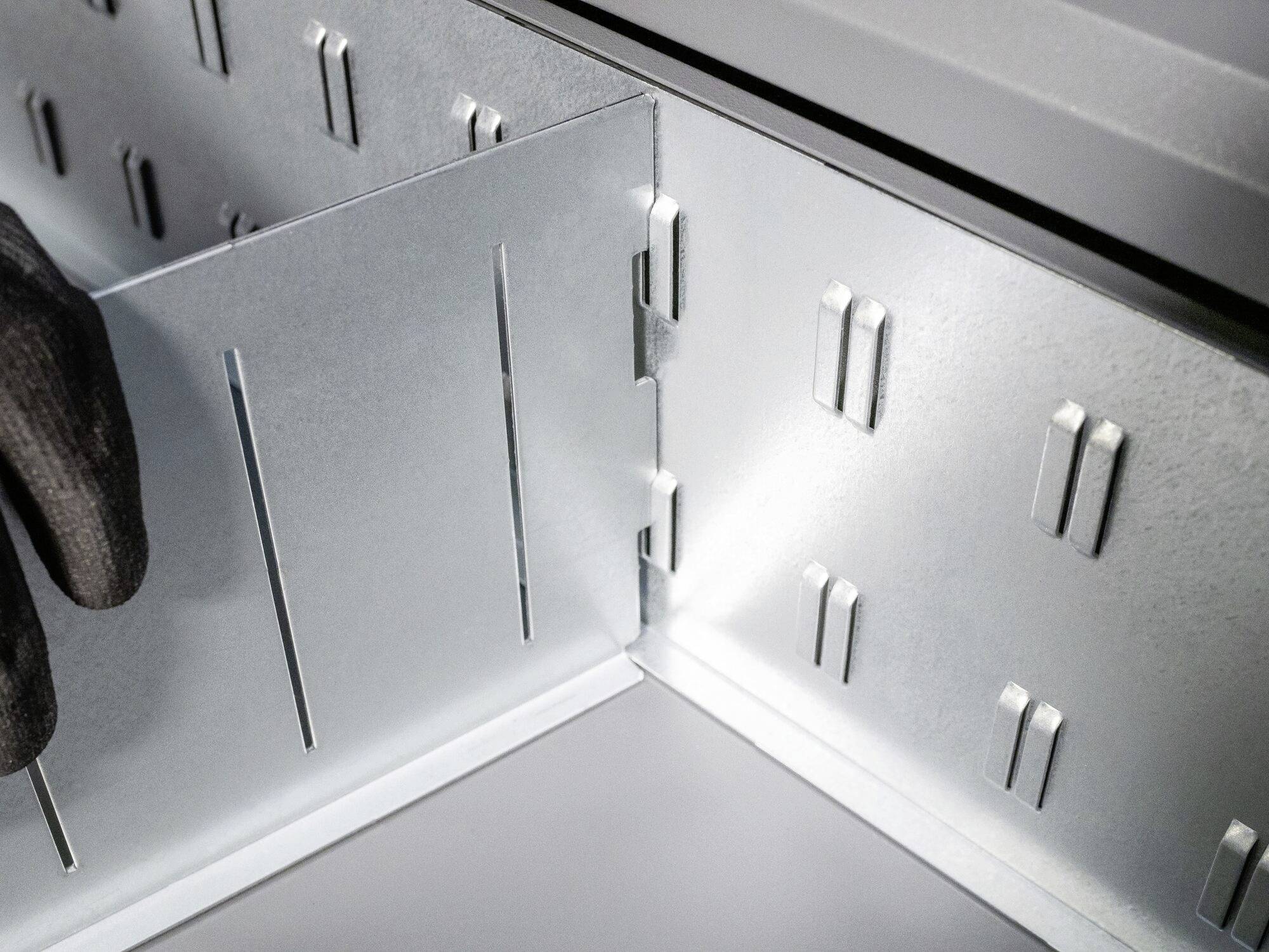 Metal containers with plug connections. A black glove touches the edge of the connections, forming a stable structure.