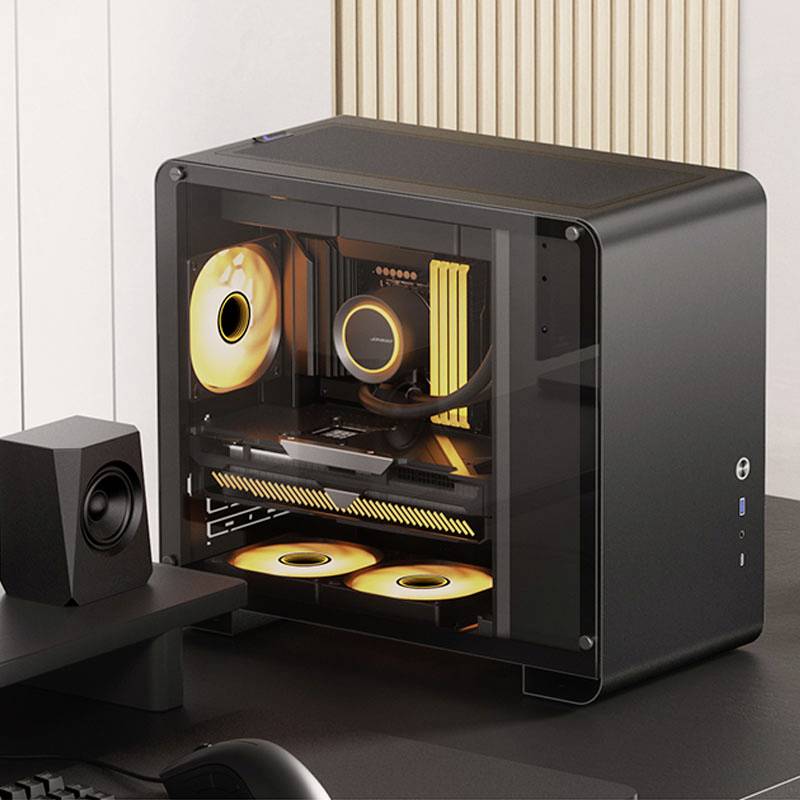 A stylish black PC sits on a desk, with a transparent front panel and orange-illuminated fans.