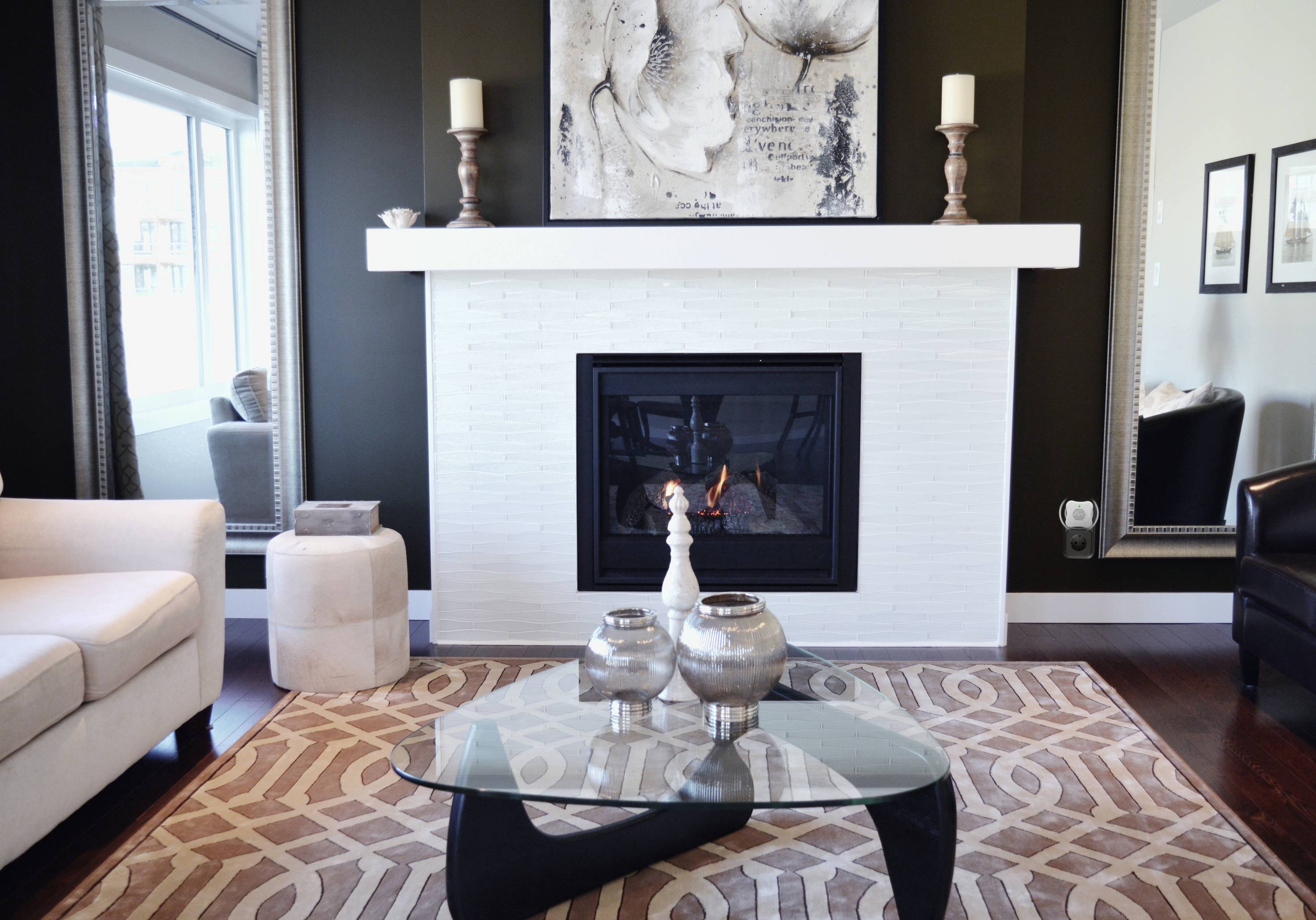 Living room with a contemporary fireplace. White brick surround, with artwork above. Glass coffee table with decorative items in front.
