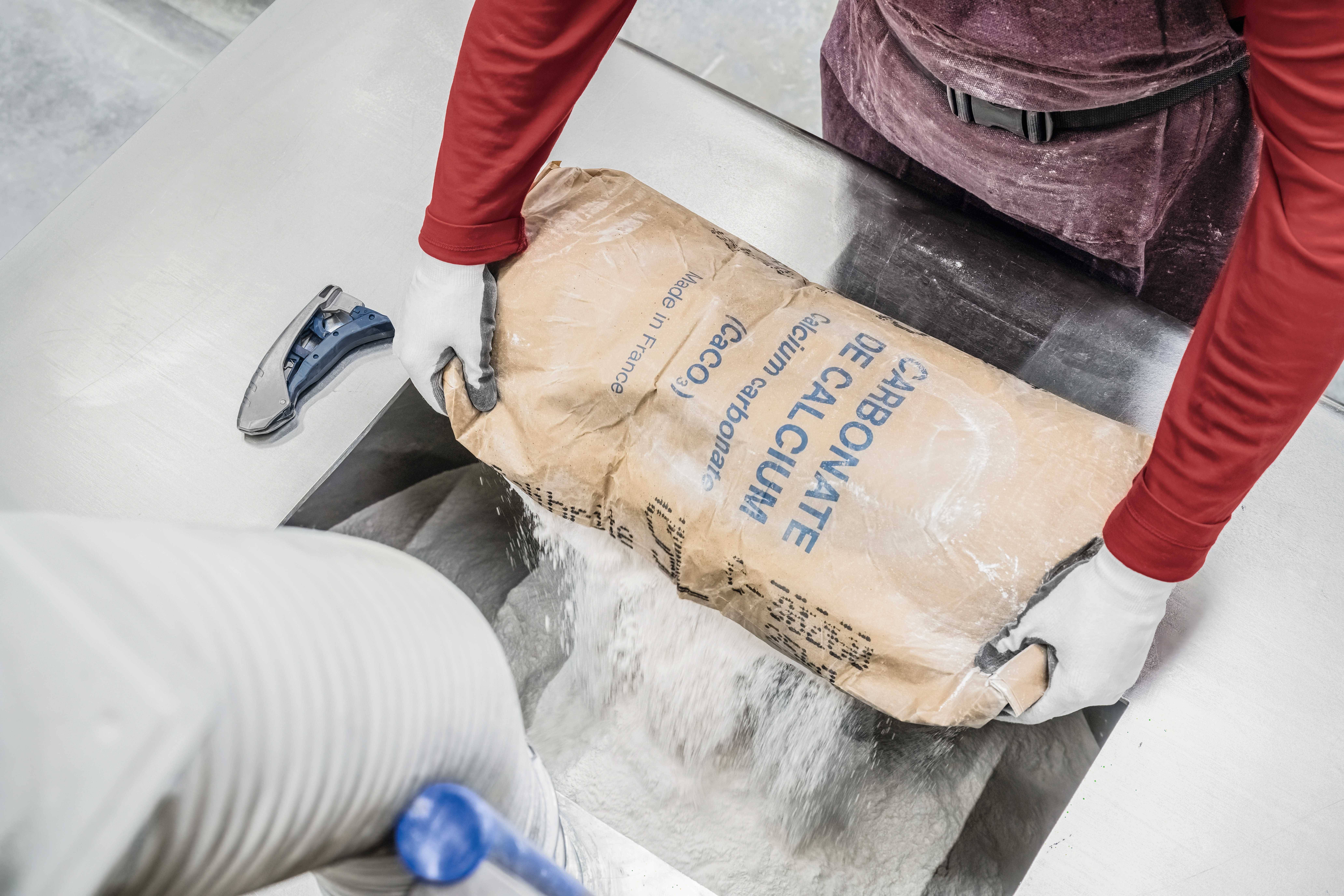 Worker pours calcium powder from a sack into a machine.