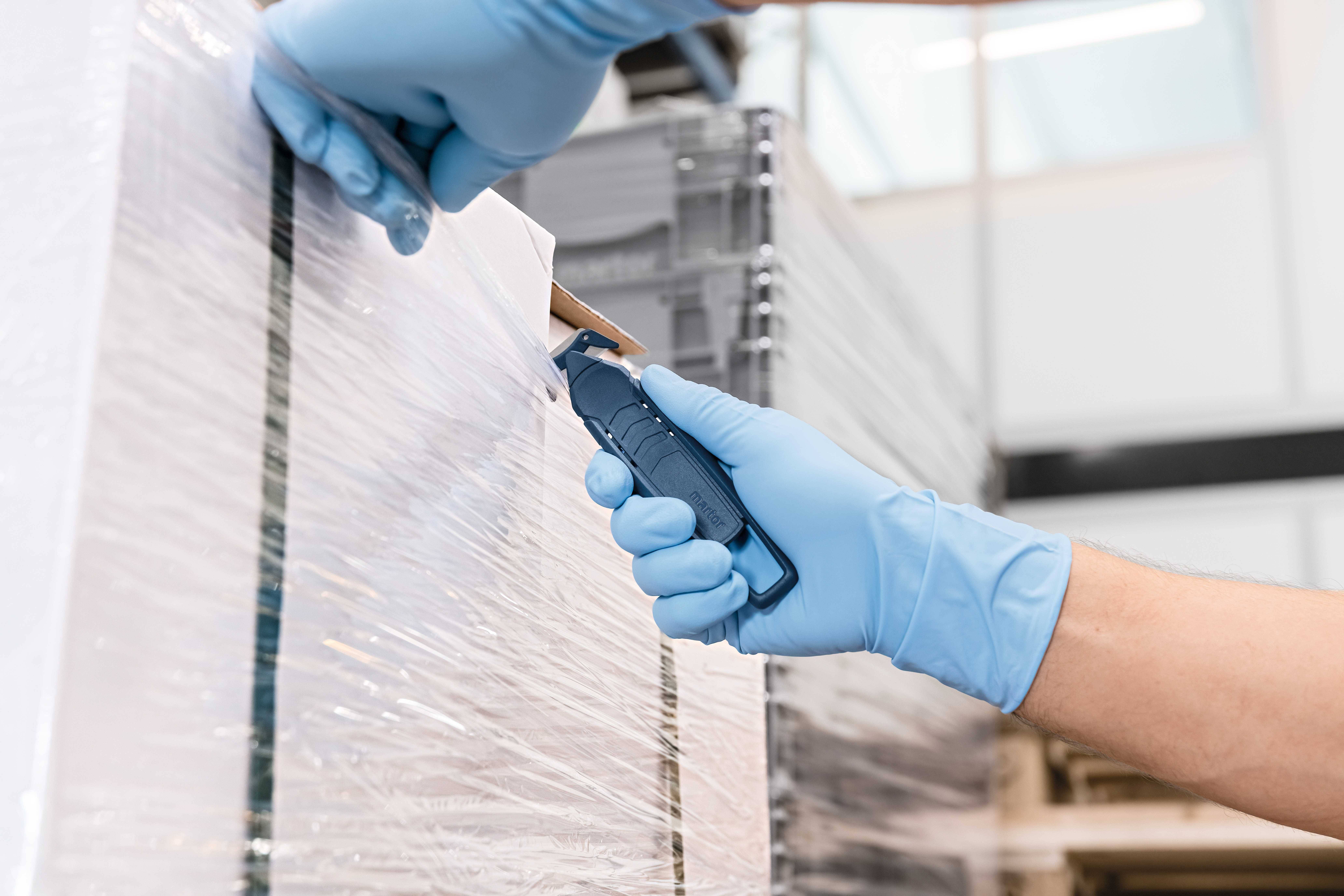 A person wearing blue gloves is cutting plastic film from a pallet.