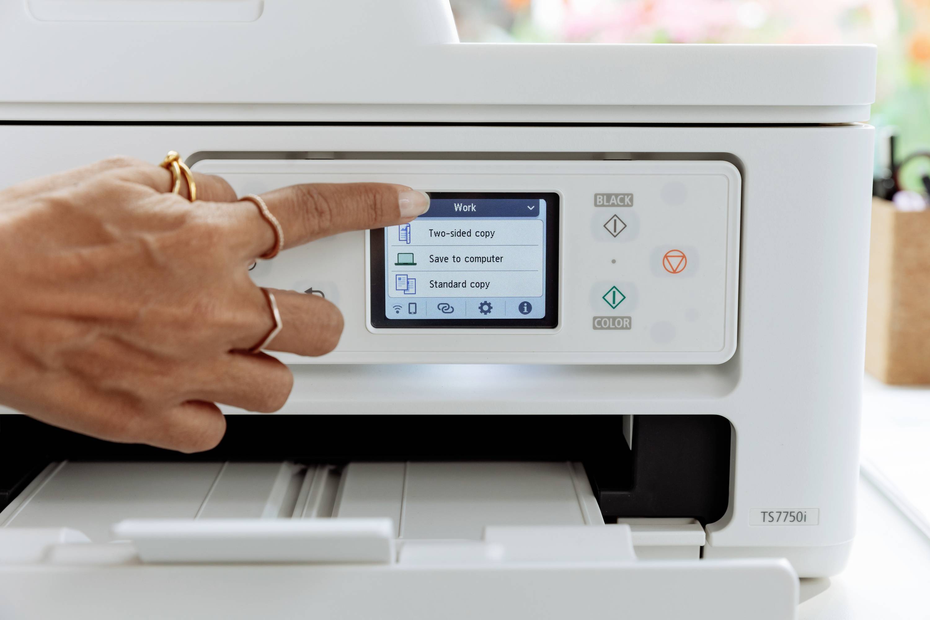 A hand is operating the touchscreen of a white printer. On the screen, options such as 'Double-sided Printing' and 'Save to Computer' are visible.