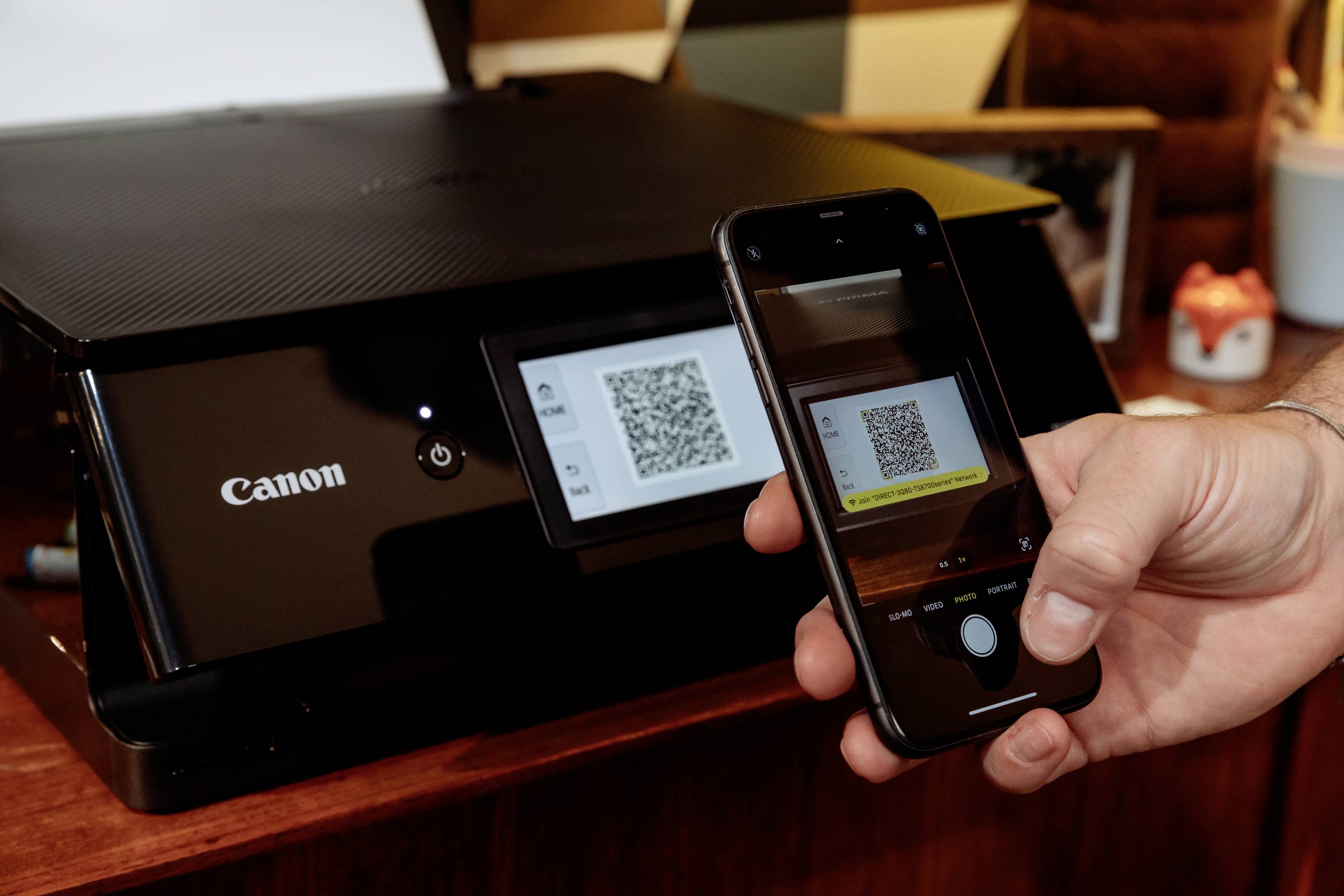 Hand holding smartphone, scanning QR code on printer display. Printer in black, close-up image of technology in use.