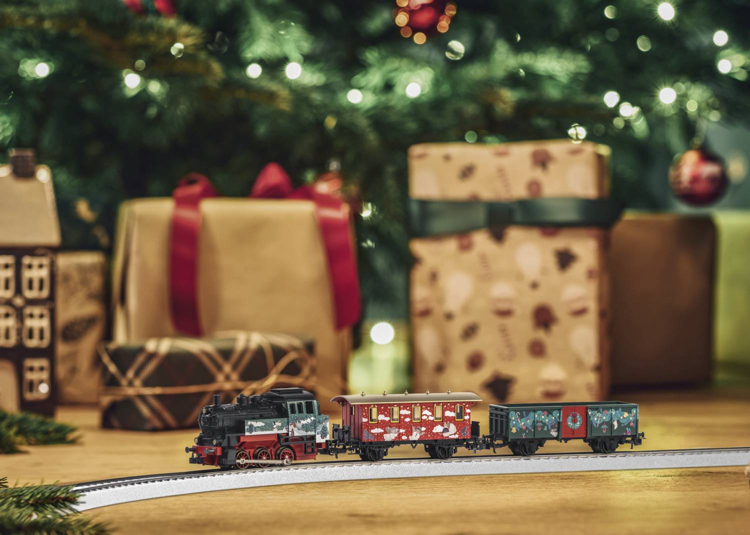 A toy train travels in front of a decorated Christmas tree. Gifts with ribbons can be seen in the background.